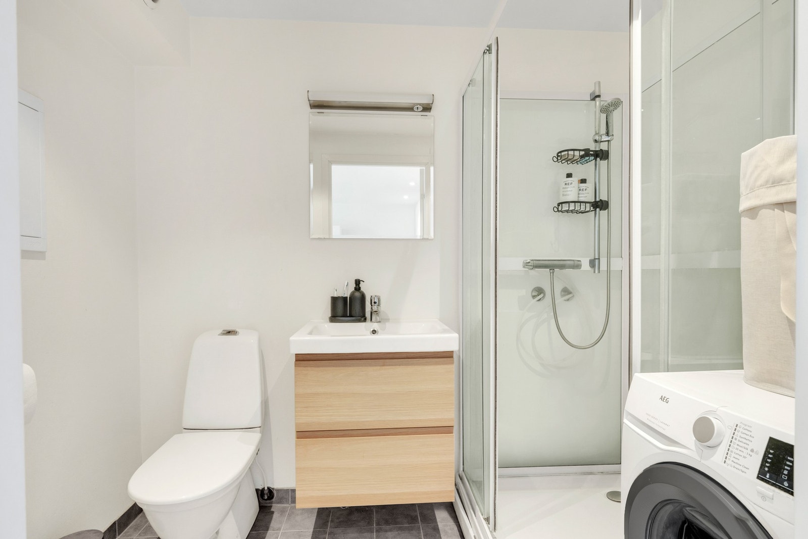 Bad med flislagt gulv, moderne innredning, dusjhjørne, WC og opplegg for vaskemaskin. Galleribilde