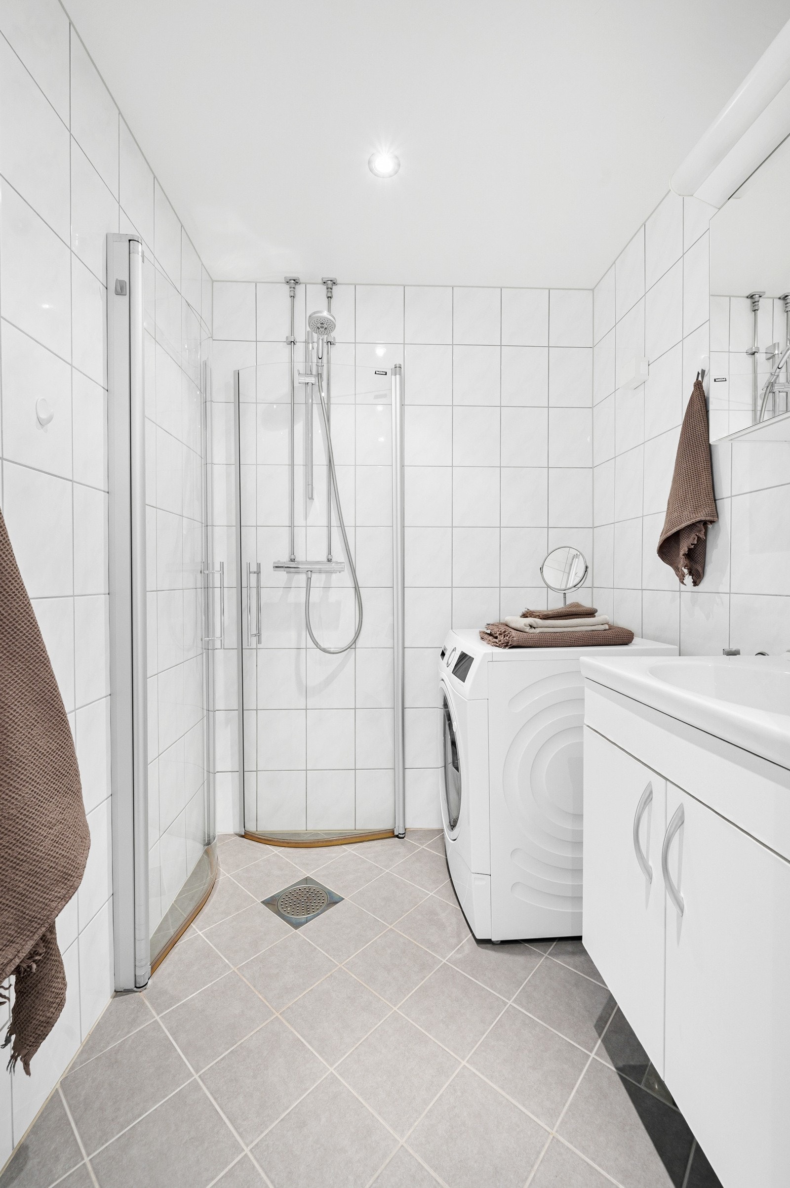 Fint og tidløst bad fra 2013 med varmekabler, opplegg for vaskemaskin, servantskap med oppbevaringsskuffer og dusjsone med innfellbare glassdører. Galleribilde