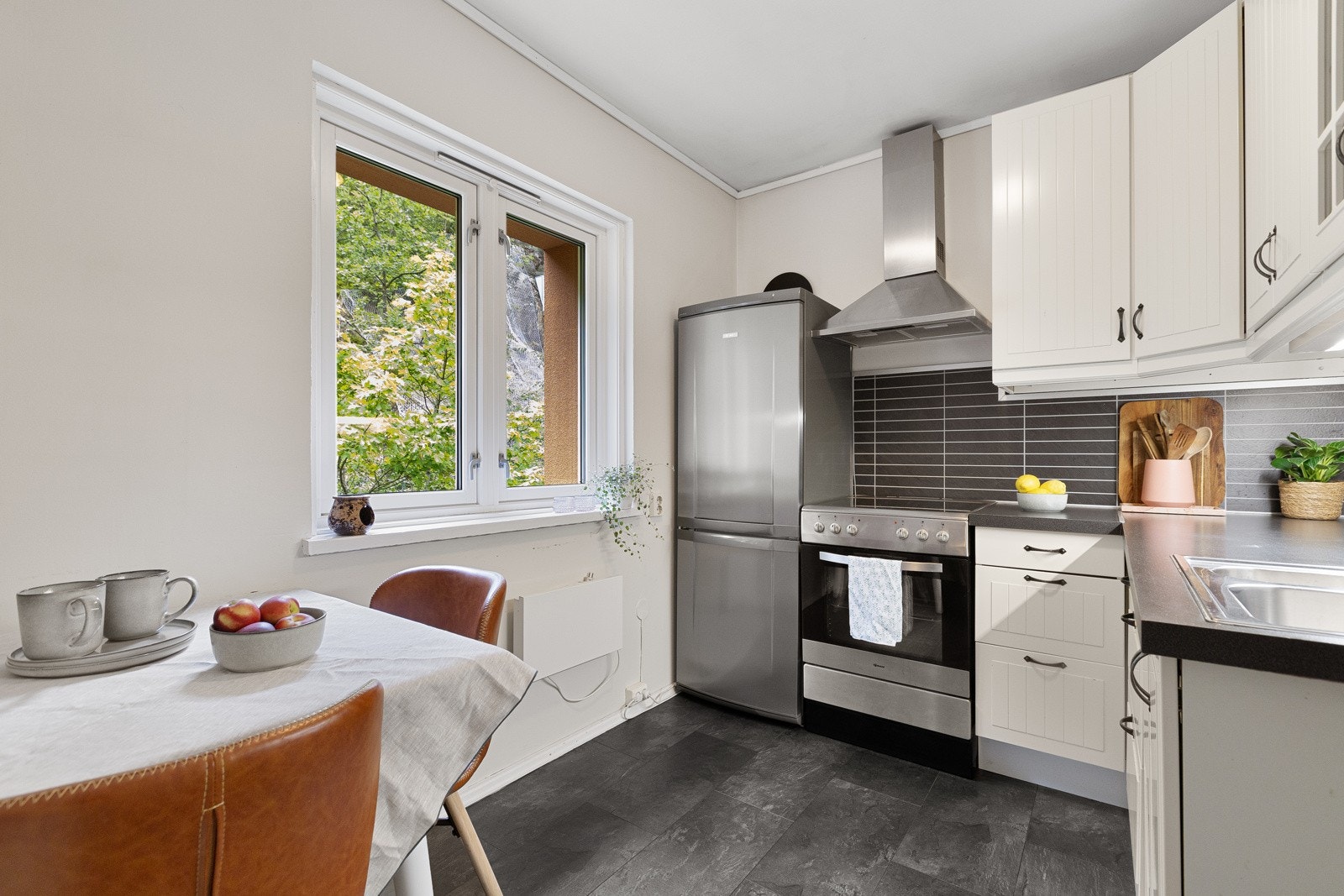 Lyst og pent kjøkken med flislaminat på gulv og malte overflater. Innredningen er fra Ikea og har profilerte fronter med to stk. glassfronter i overskap, og benkeplate av laminat. Galleribilde