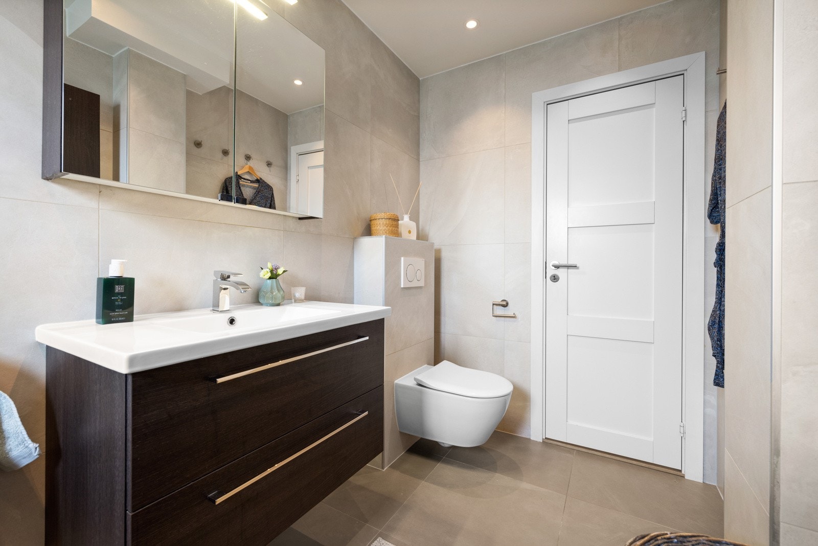 Videre har badet et vegghengt toalett og et dusjhjørne med regnfallsdusj bak en glassvegg Galleribilde