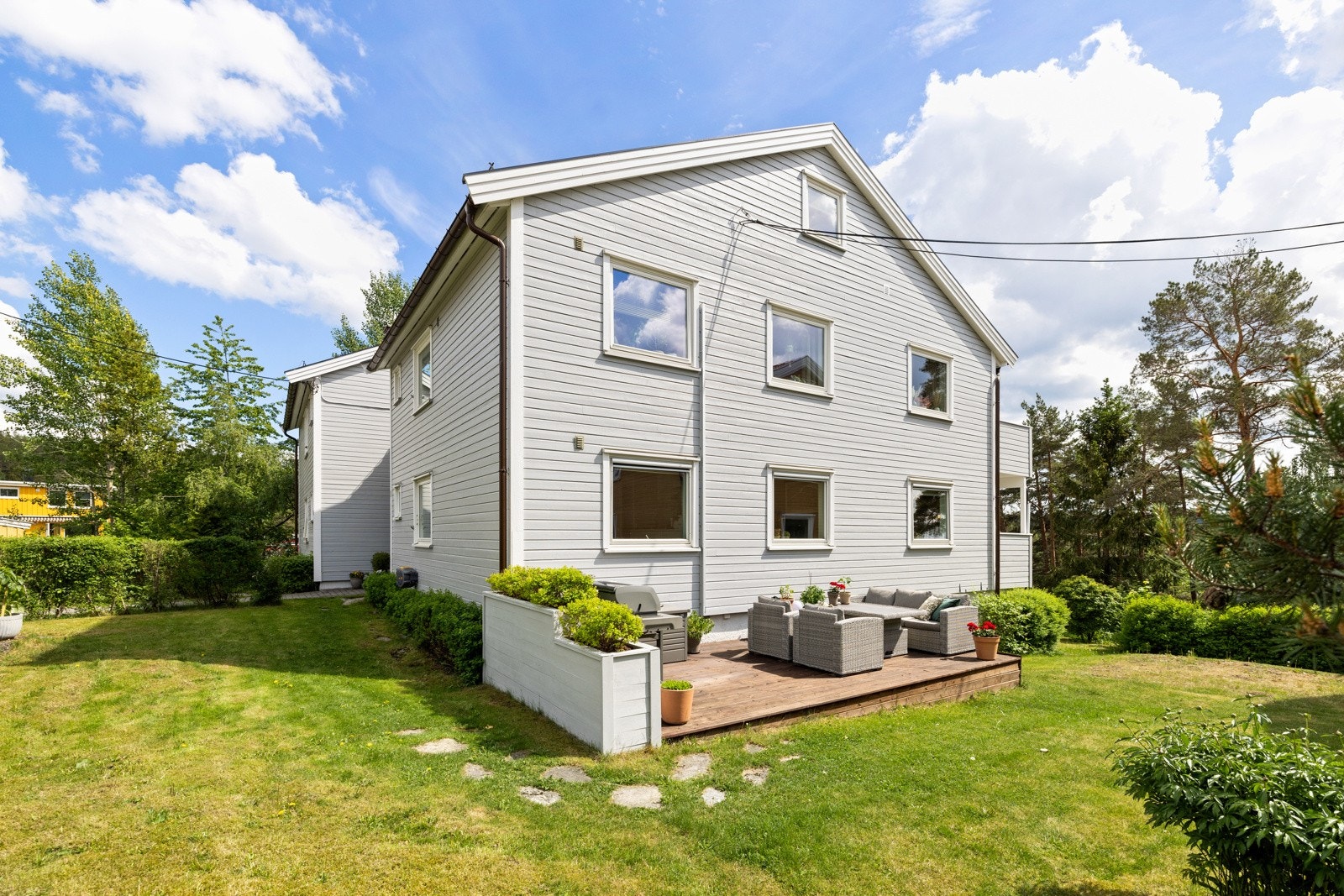 Fellestomten er pent opparbeidet med gressplen, hekk, frodige prydbusker og steinbelagt adkomst Galleribilde