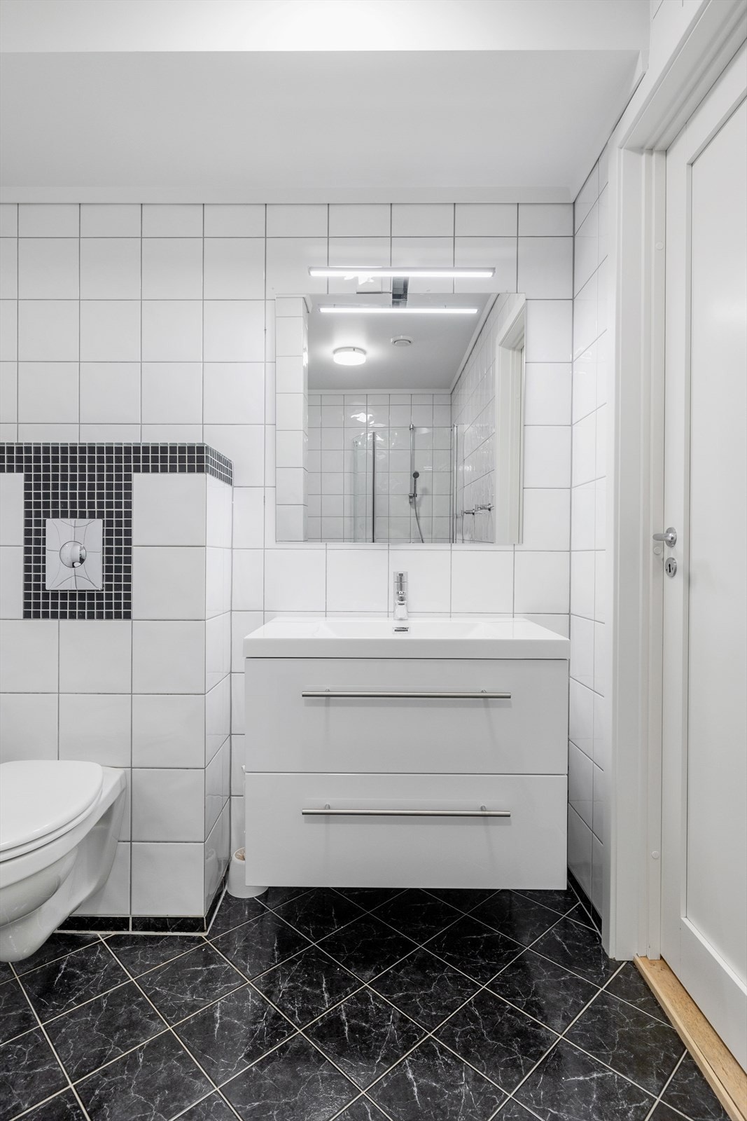 Badet er enkelt innredet med vegghengt toalett, dusjhjørne og servantinnredning med skuffer Galleribilde