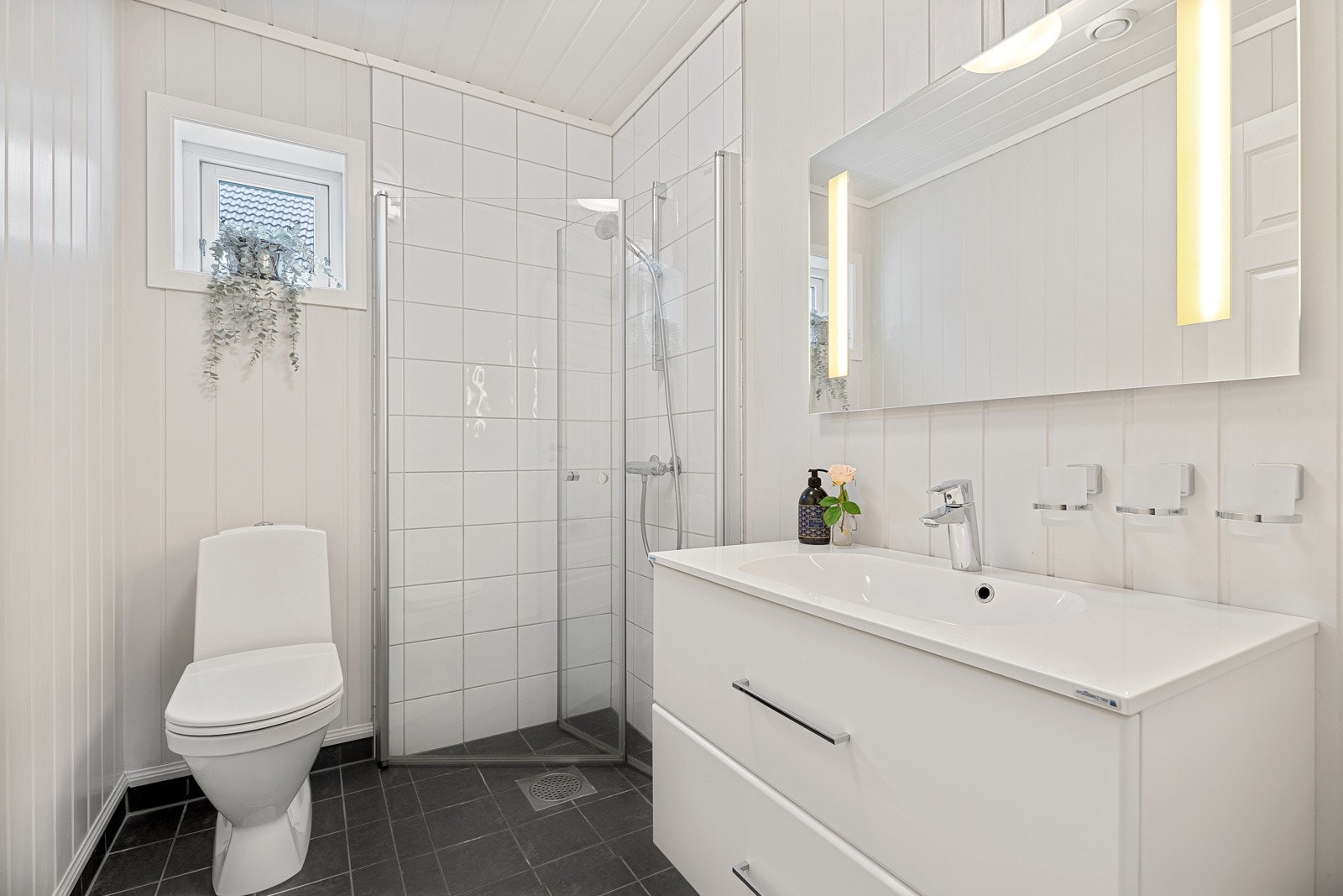 Delikat baderom med gulvstående toalett, dusjhjørne og servant med speil. Galleribilde