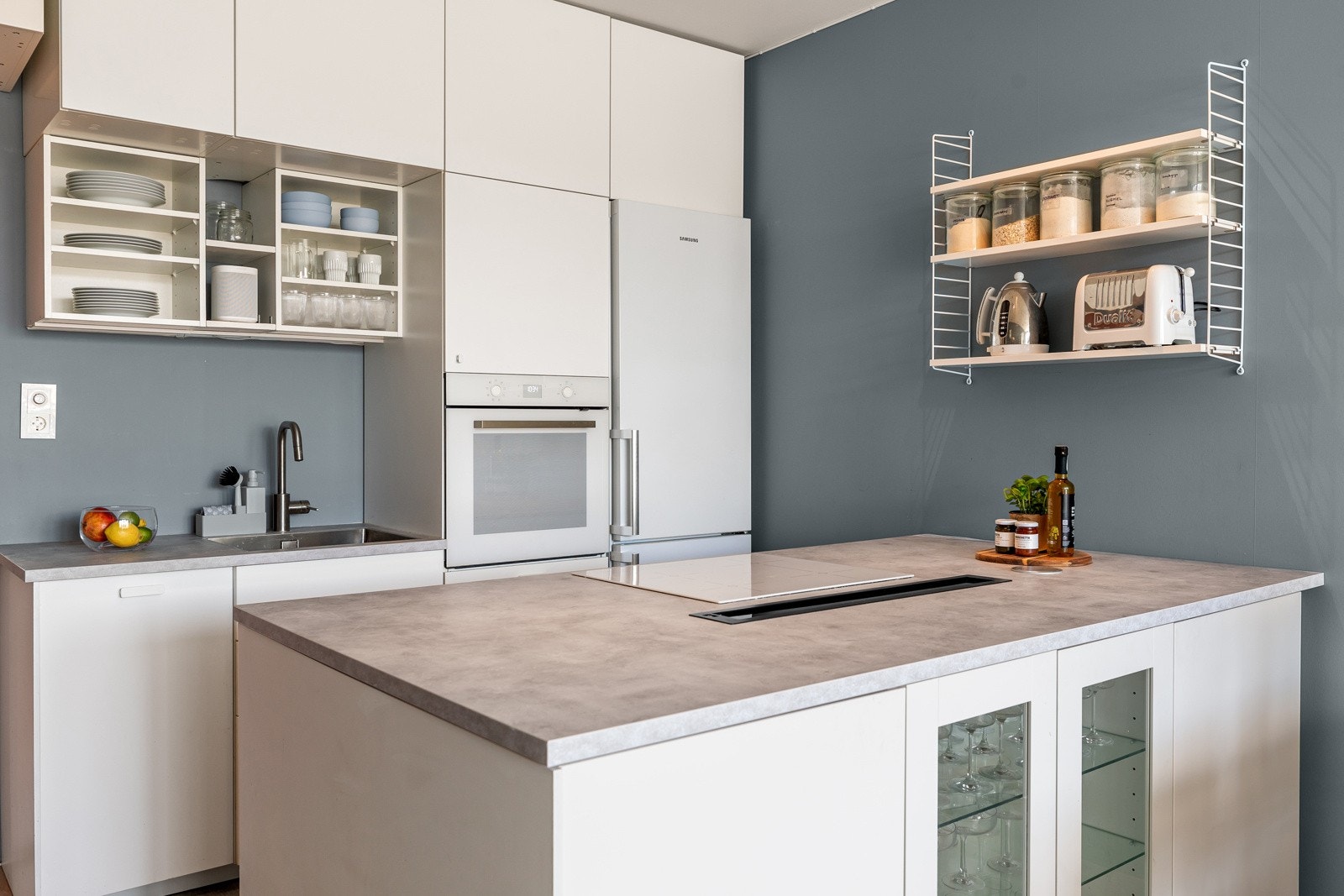 Kjøkkenet er innredet med vite slette fronter, overskap med benkebelysning og kjøkkenøy. Lysgrå laminat benkeplate med planlimt vask og ett-greps armatur i børstet stål Galleribilde