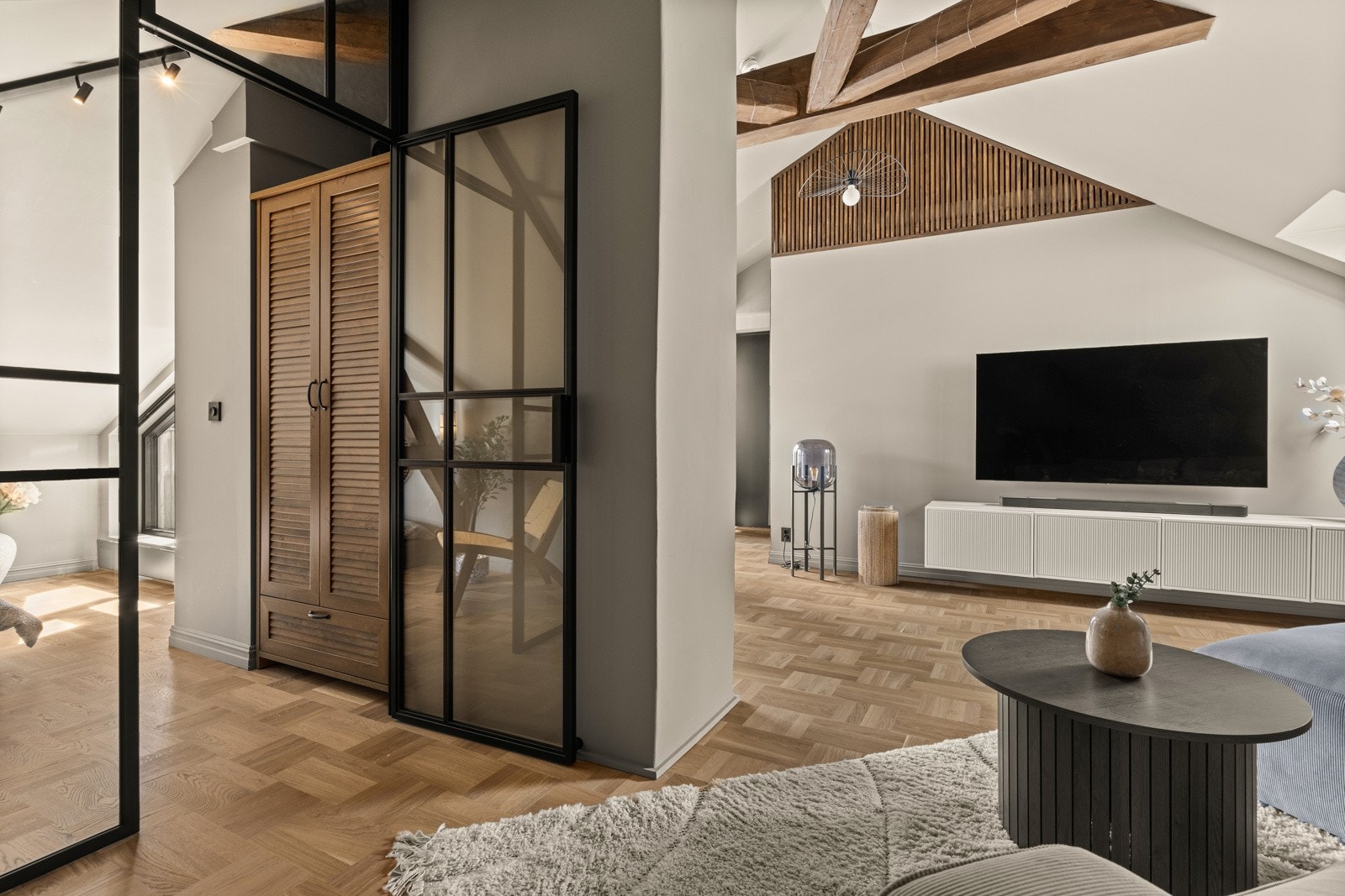 Loftstuen kombinerer den klassiske sjarmen med originale, synlige trebjelker og det moderne preget med spiler samt glassvegger med sorte rammer. Galleribilde