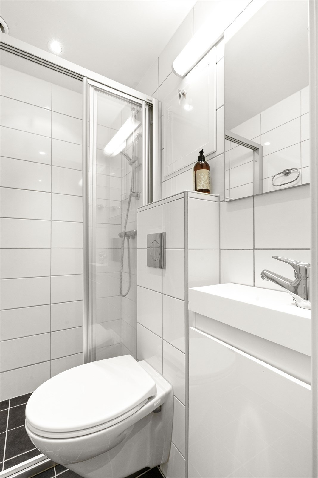 Dusjinnredning med gulvsokkel og skyvedør, vegghengt toalett og servantskap. Galleribilde