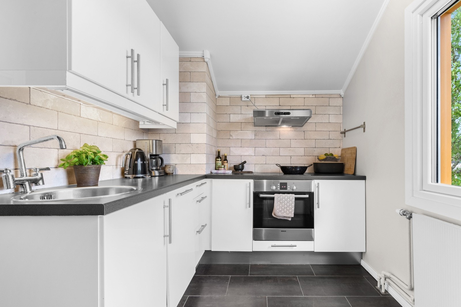 Kjøkkenet er utstyrt med fliser på vegg, integrert platetopp, oppvaskmaskin og nedfelt kum i rustfritt stål Galleribilde