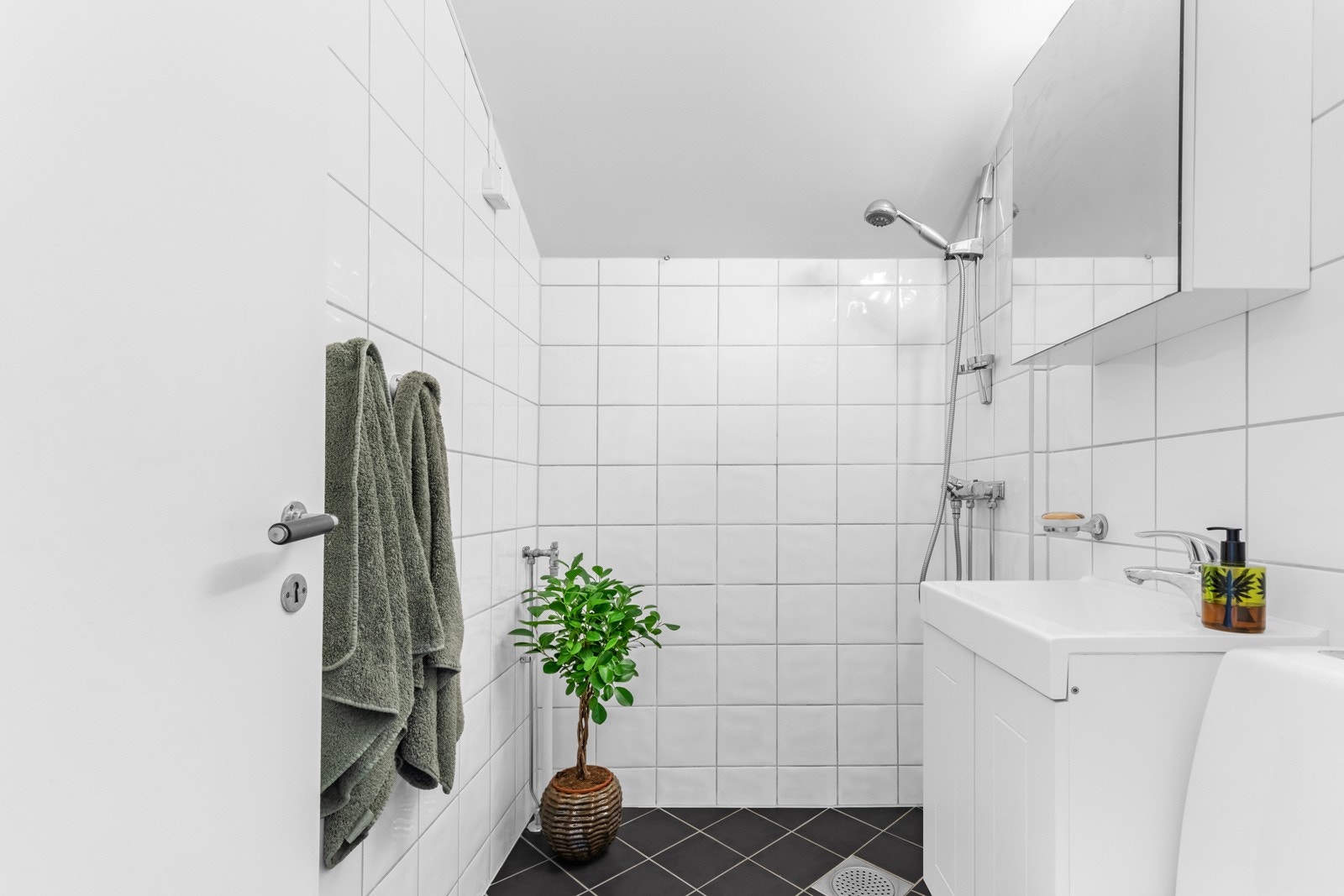 Videre er badet utstyrt med servantskap med profilerte fronter og heldekkende servant, speilskap og lysarmatur, gulvmontert klosett og dusjhjørne Galleribilde