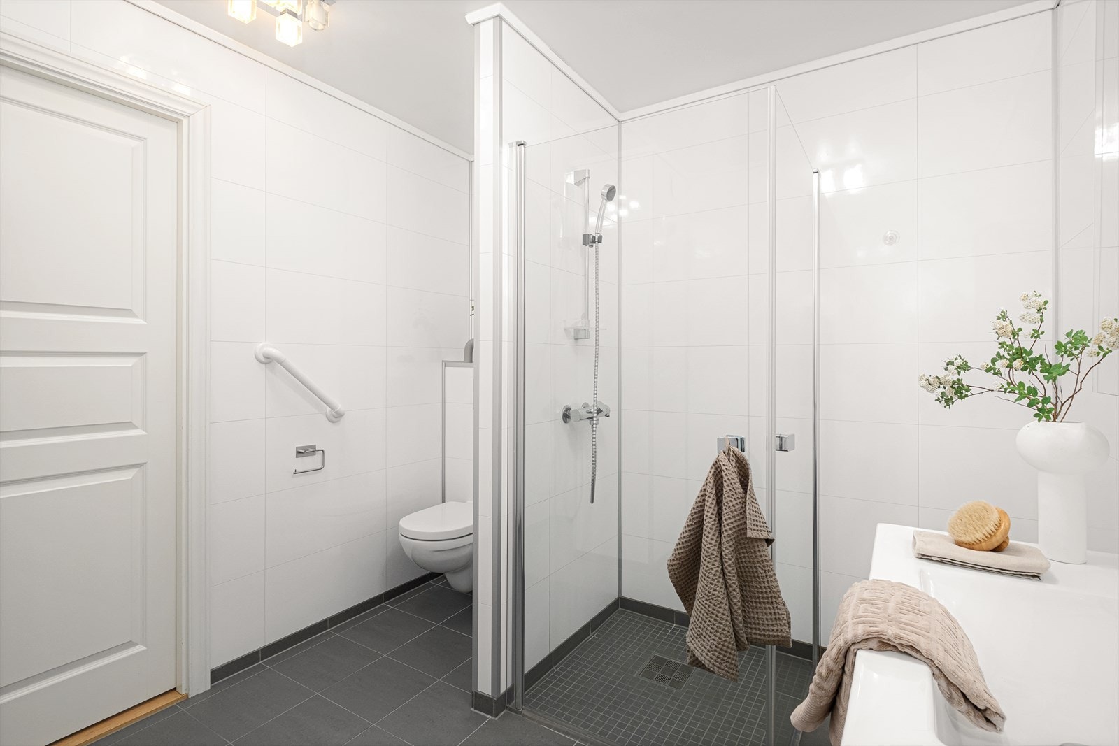 Badet er innredet med vegghengt toalett, helstøpt servant med skuffer, dusjdører i klart glass og opplegg for vaskemaskin. Galleribilde