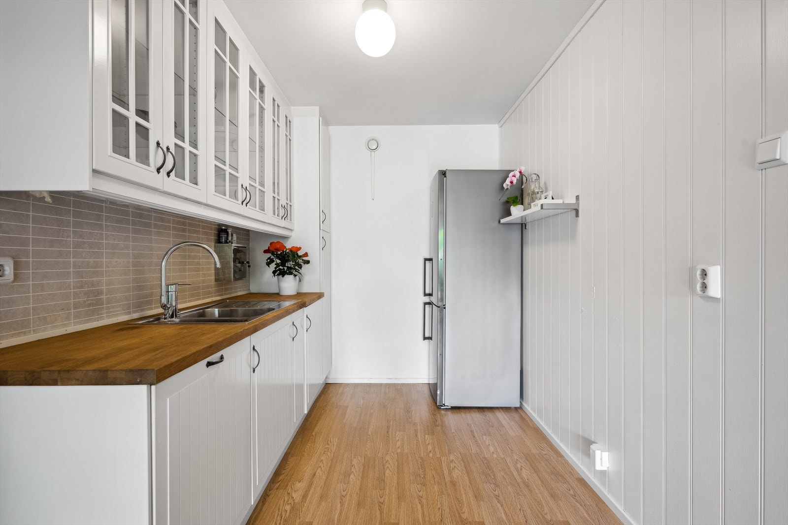 Kjøkkeninnredning med profilerte fronter og vitrineskap, plater og benkeplate med nedfelt oppvaskkum m/ bl.batteri. Kjøkkenet er utstyrt med oppvaskmaskin og plass til frittstående komfyr og kjøl/frys. Galleribilde