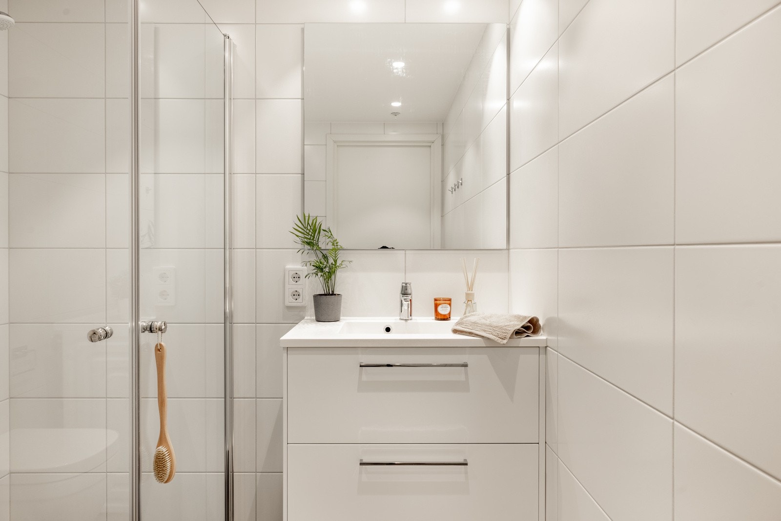 Badet er innredet med vegghengt toalett, dusj med innfellbare glassvegger og servantmøbel med skuffer og overhengende speil. Galleribilde