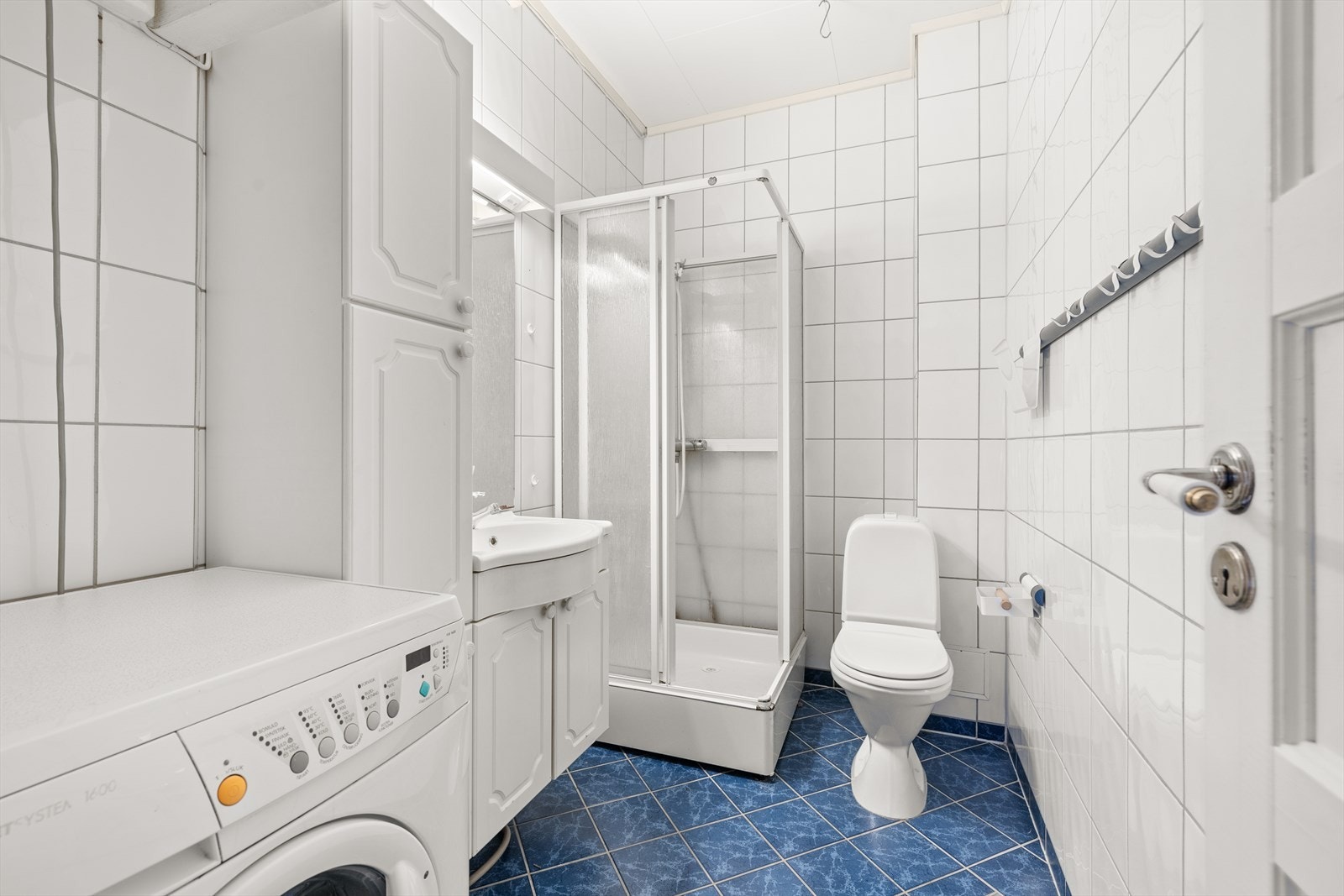 Det fliselagte baderommet er utstyrt med dusjkabinett, toalett, servant med gode oppbevaringsskap og opplegg for vaskemaskin. Galleribilde