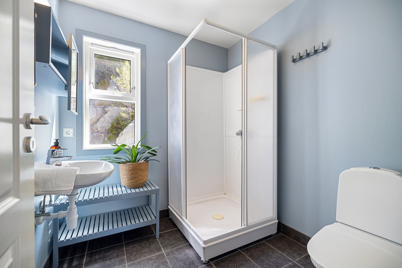 Badet i loftsetasjen har flislagt gulv med gulvvarme og malte veggflater. Rommet inneholder vegghengt servant med ett-greps armatur, speil med overlys og stikkontakt over servant, dusjkabinett med dusjarmatur, samt gulvstående toalett. Galleribilde
