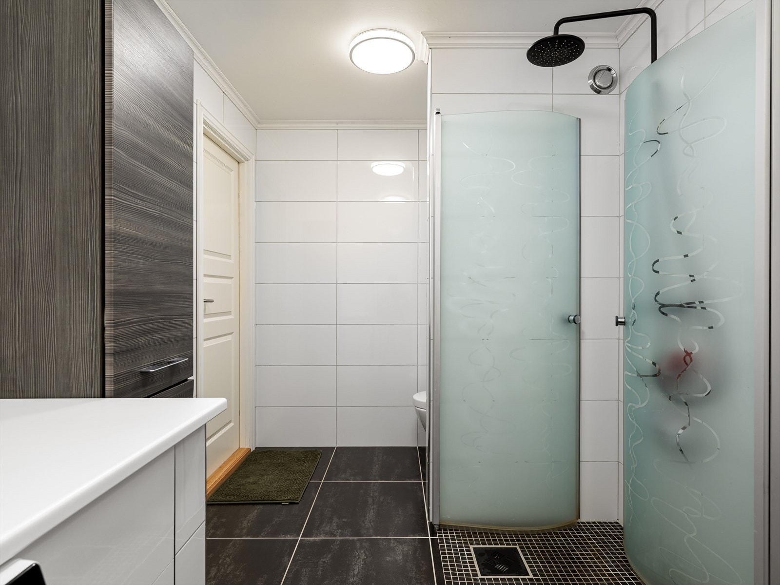 Vannfallsdusj med mosaikk på gulv. Helfliset baderom med oppbevaring i både seksjon, speilskap og ekstra veggskap. Arbeidsbenk og skap til skittentøy. Galleribilde
