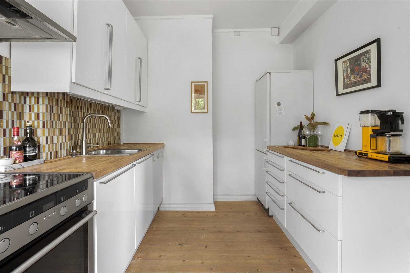 Pen kjøkkeninnredning med heltre benkeplate. Flislagt veggflate over benkeplate med komfyr og kum. Galleribilde