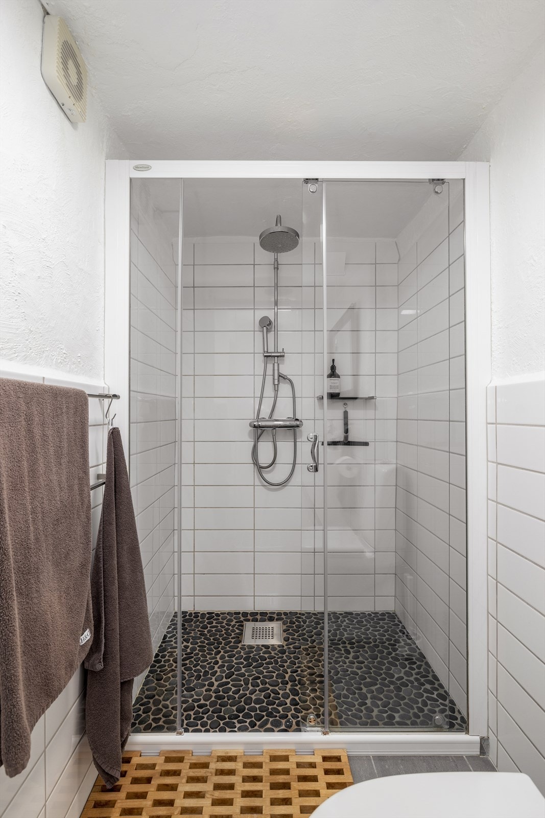 Åpen dusjløsning med kulestein på gulv og flislagte veggflater, samt dusjdører. I tillegg servantinnredning med skuffer og heldekkende servant. Galleribilde