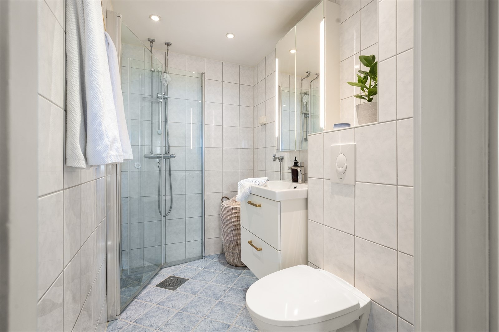 Lyst flislagt bad med downlights i tak og varmekabler på gulv. Badet ble pusset opp i 2009/2011 i regi av borettslaget, og ble oppgradert med ny servantinnredning og speilskap i 2021. Galleribilde