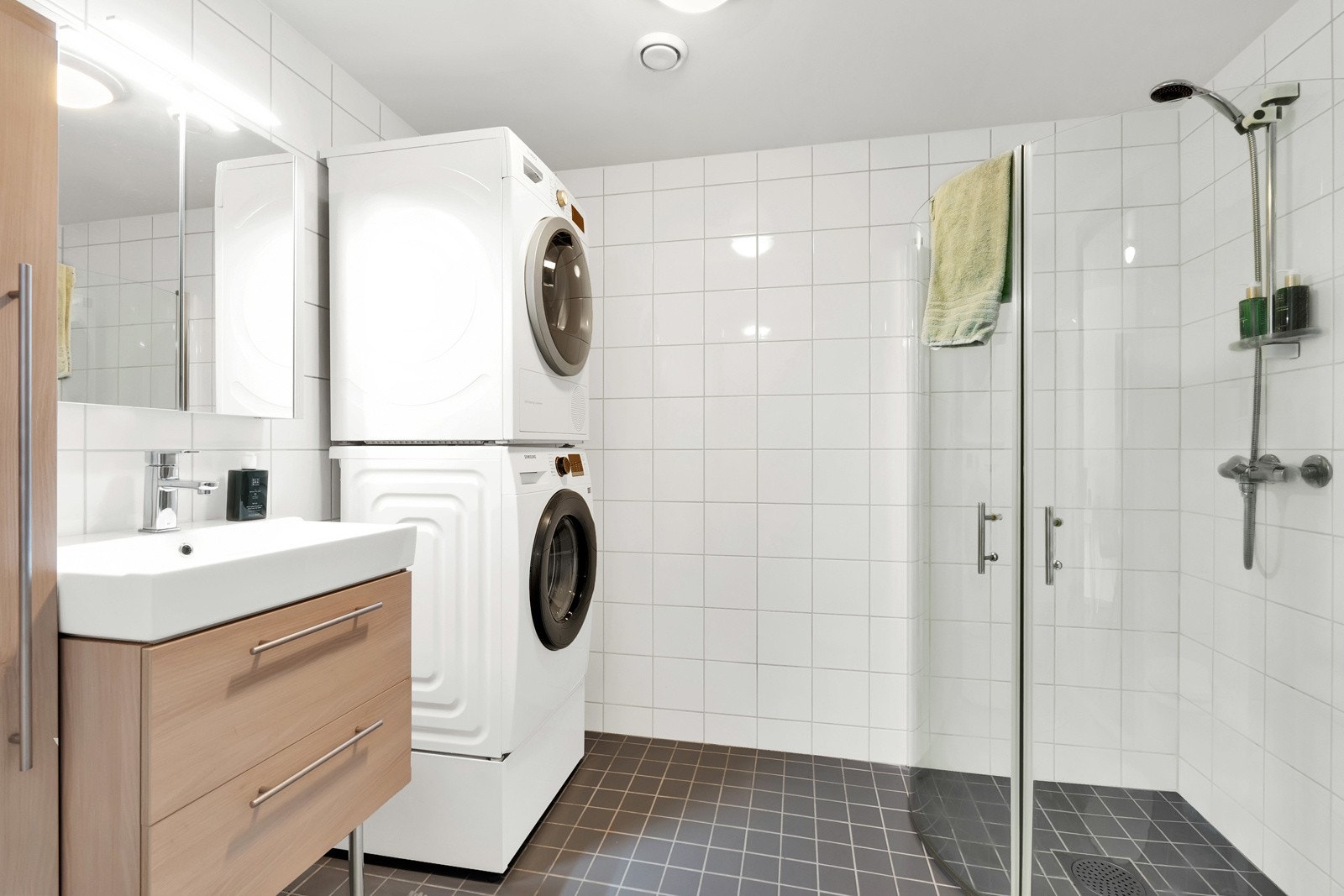 Stort bad med fliselagt gulv og vegger, hjørnedusj, gulvvarme og opplegg for vaskemaskin/tørketrommel. Galleribilde