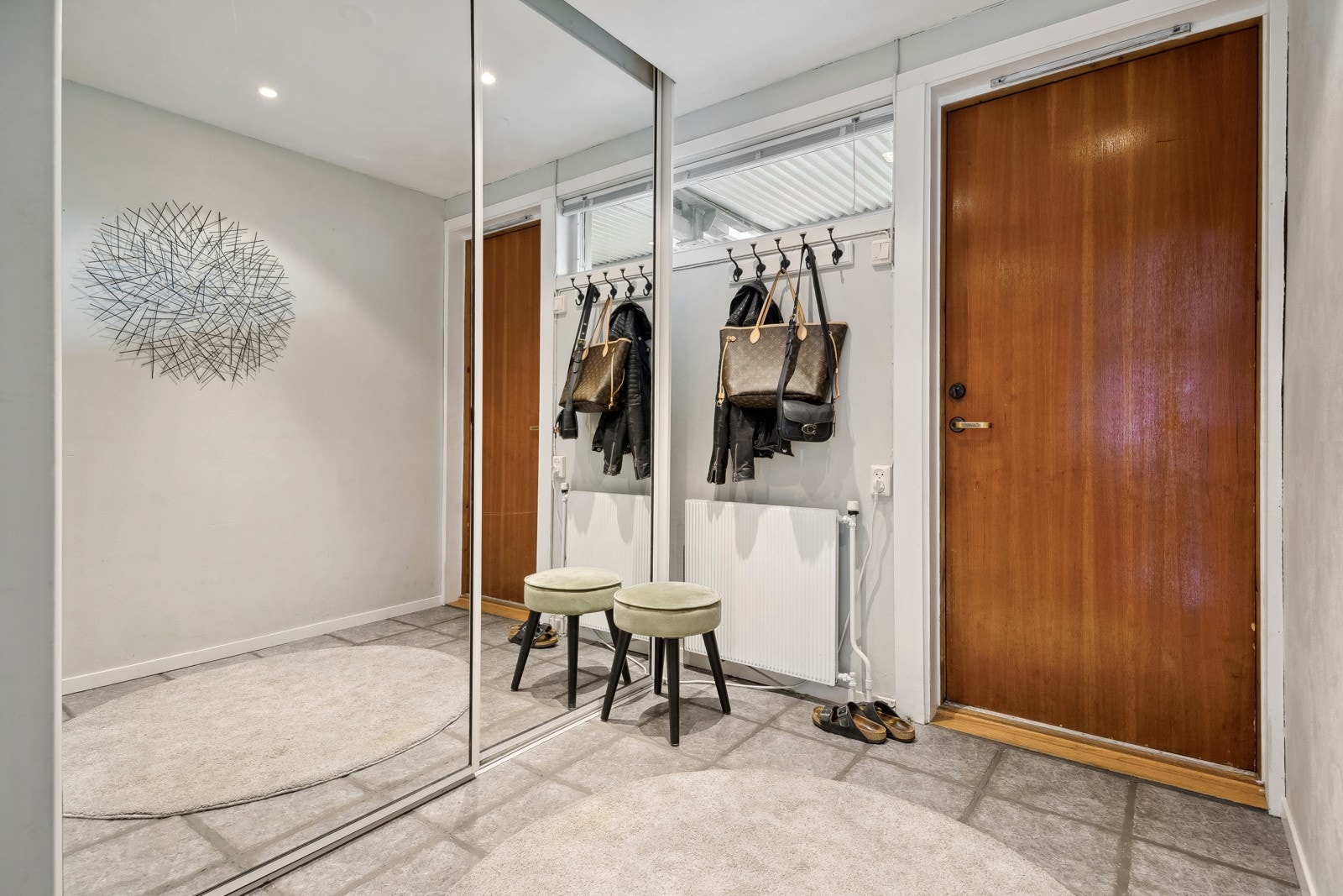 Du kommer inn i boligen via en romslig, flislagt entré med praktisk, stor og pen skyvdørsgarderobe med speilfronter. Fliser på gulv. Galleribilde