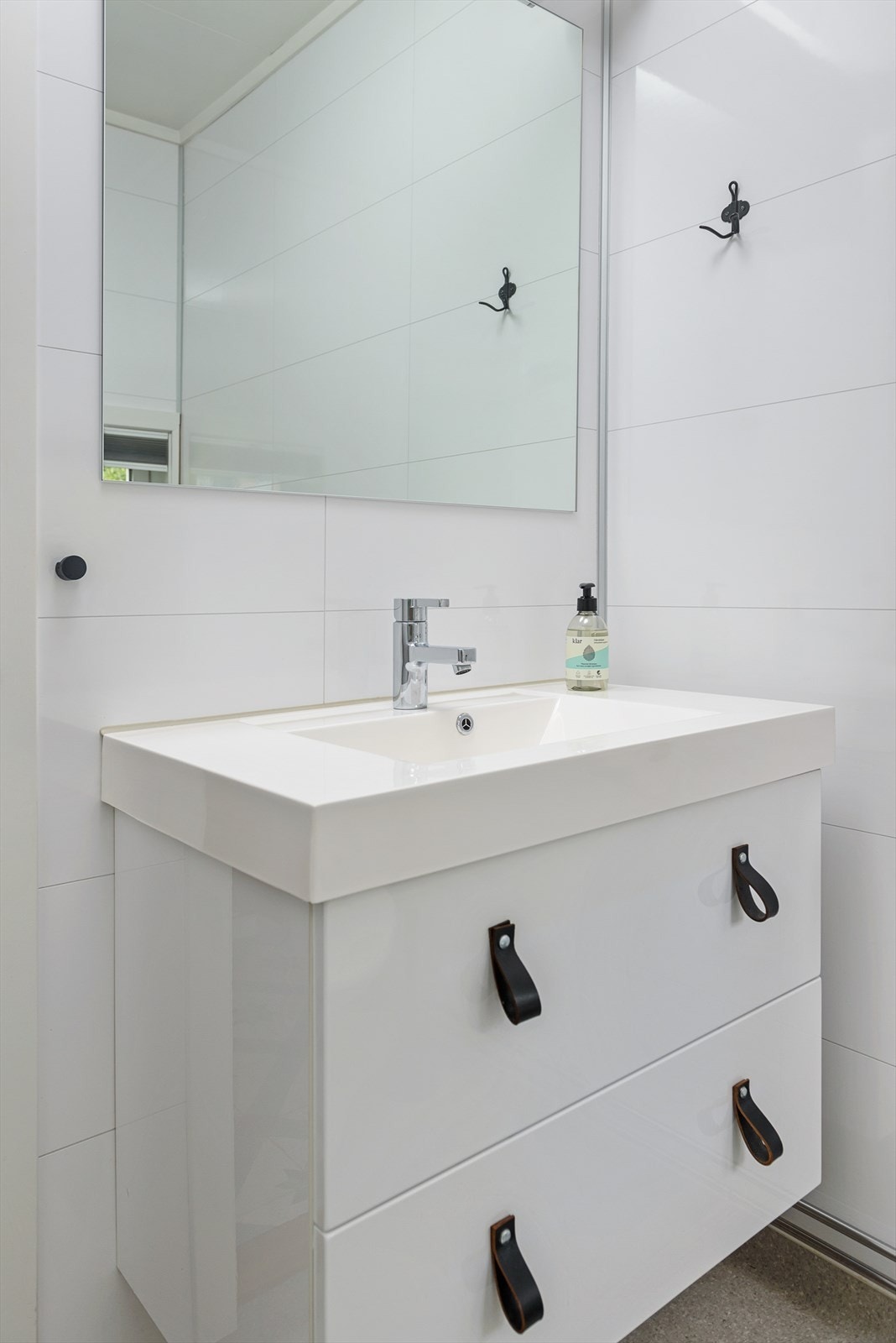 Badet inneholder en nyere servant med skuffeseksjon, speil med tilhørende belysning, dusjvegger og gulvmontert WC. Galleribilde