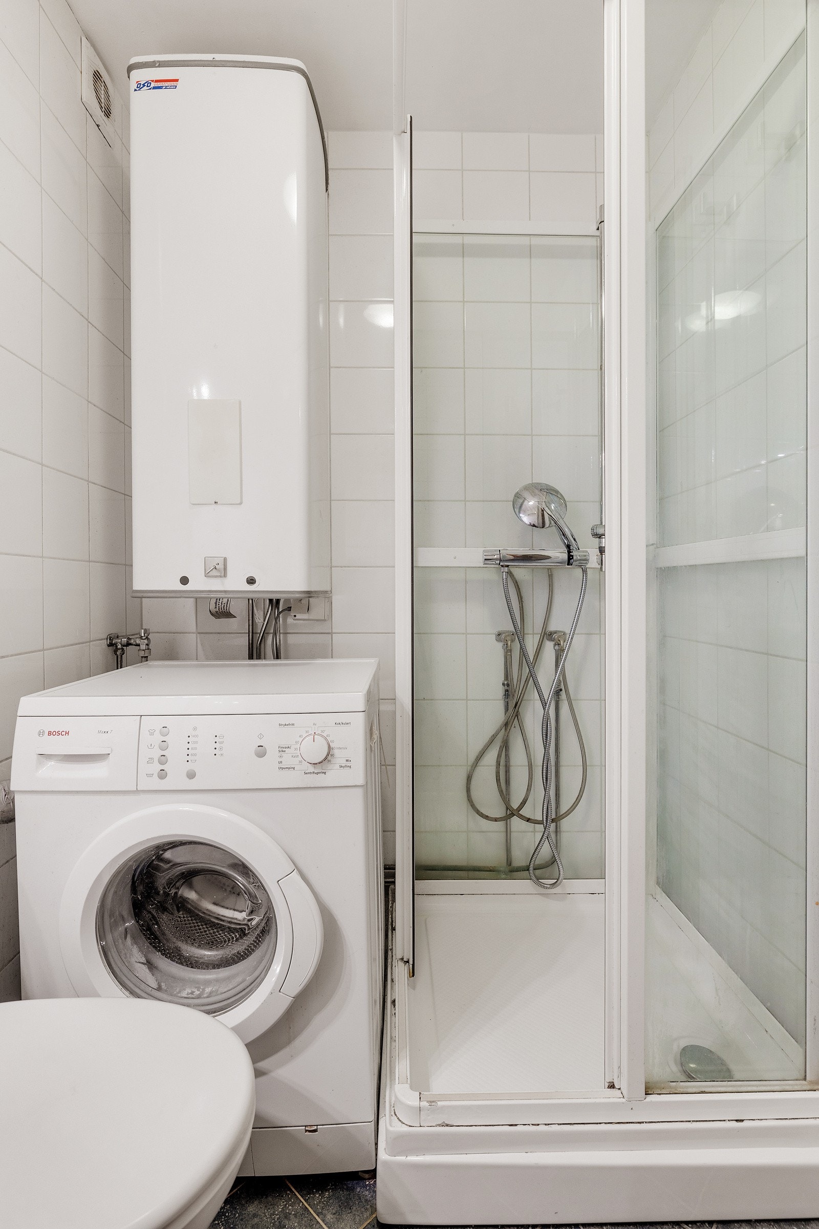 Badet har toalett, dusjkabinett og opplegg for vaskemaskin under en eldre varmtvannsbereder på 100 liter. Galleribilde