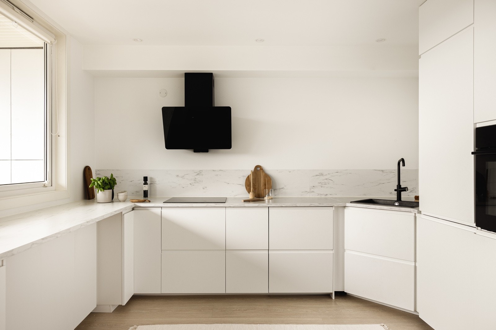 Kjøkkeninnredningen er stilren med hvite slette fronter og lys benkeplate med nedfelt vask i sorte detaljer. Galleribilde