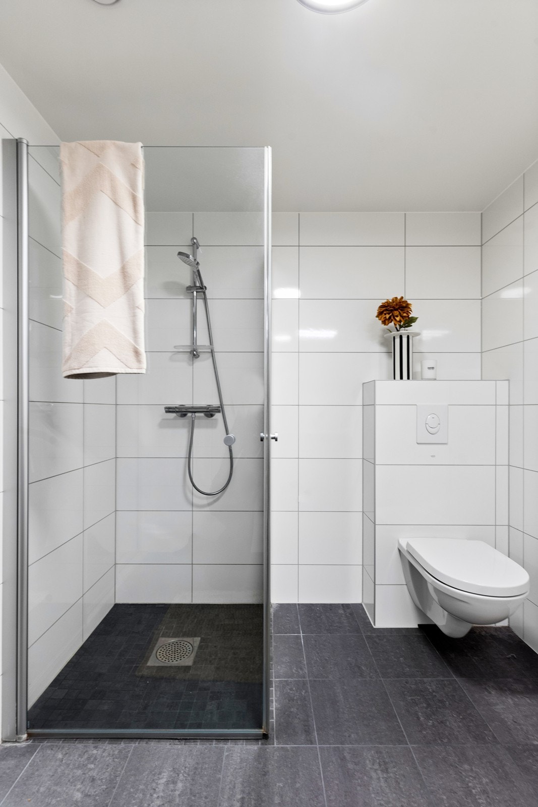 Tidløse flisevalg både på vegg og gulv med moderne løsninger med vegghengt toalett og innfellbare dusjvegger. Galleribilde