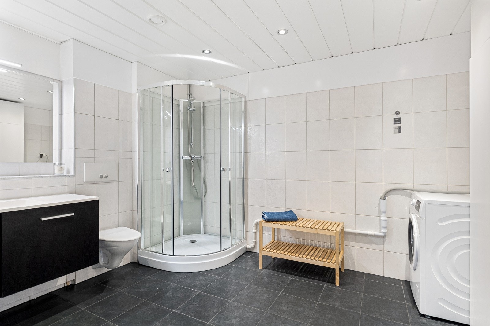 Badet inneholder servant med møblement/speil, belysning, vegghengt toalett, dusjkabinett og opplegg for vaskemaskin Galleribilde