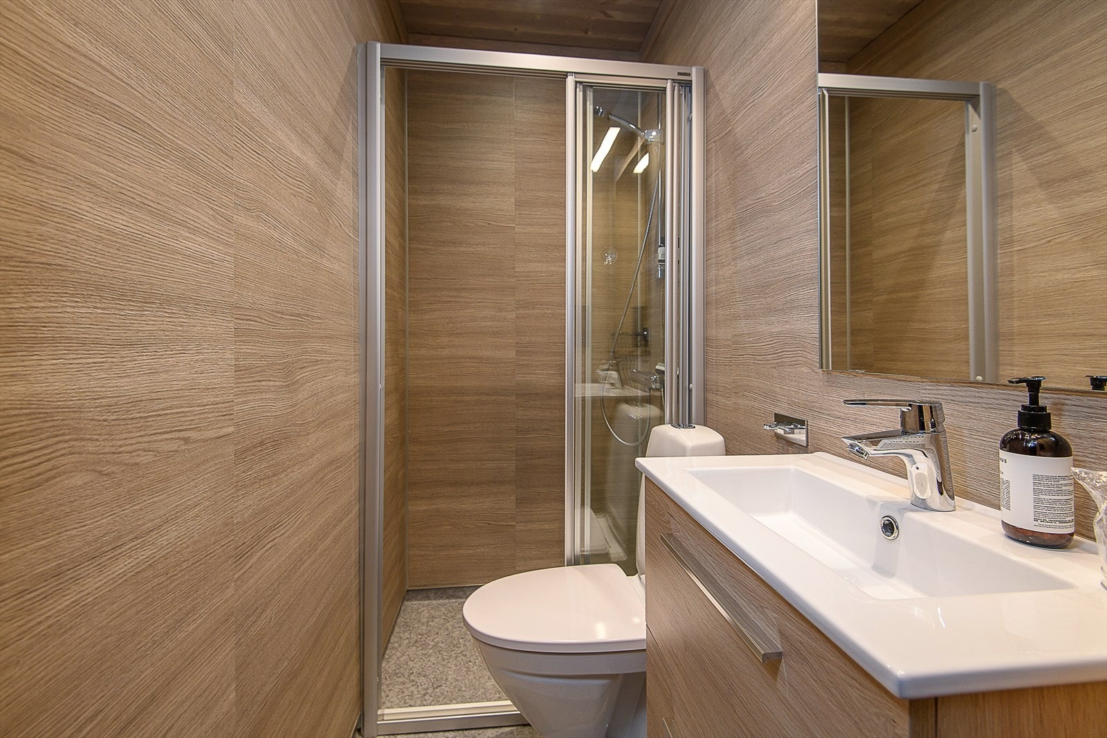 Badene er innredet med servant med underskap, speil med tilhørende belysning, dusjnisje og gulvmontert wc. Galleribilde