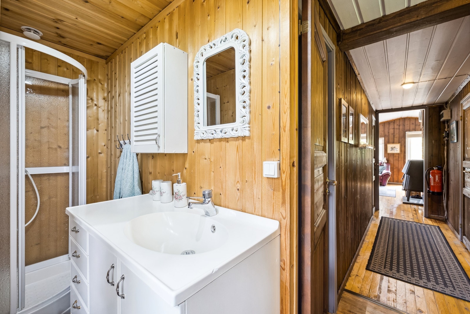 Hygienerommet har lakkert tregulv og panel på veggene. Rommet er innredet med heldekkende servant i hvit skap- og skuffeinnredning, vegghengt skap og dusjkabinett. Galleribilde