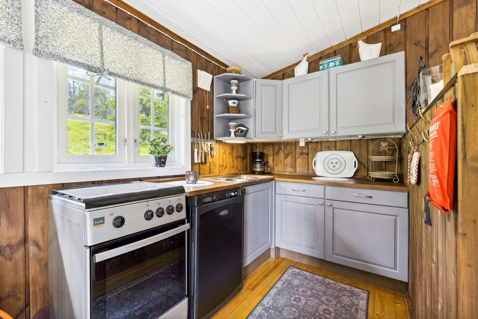 Kjøkkeninnredning med grå laminerte skrog, profilerte, laminerte fronter og heltre benkeplater. Innredningen i hjørneløsning med overskap, underskap og skuffer. Galleribilde