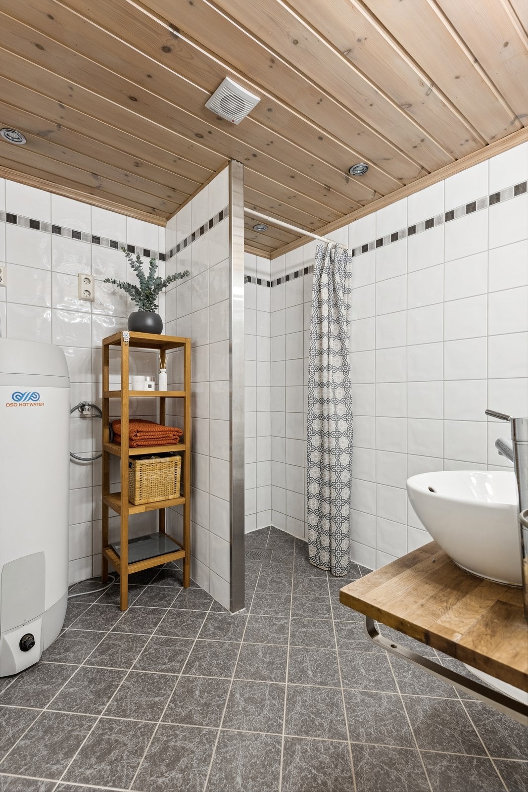 Pent og klassisk bad med opplegg for vaskemaskin, dusj, wc og vask. Varmtvannsberederen til huset er plassert i dette rommet. Galleribilde