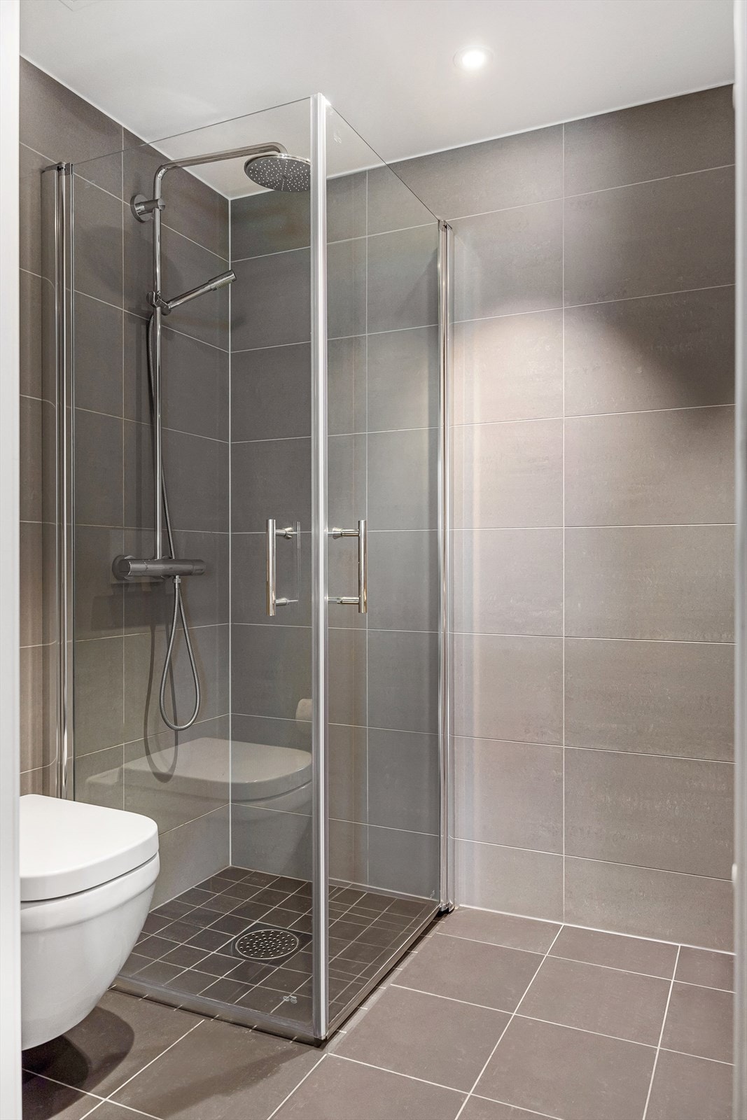 Badet er innredet med vegghengt klosett, servant med innredning, speilskap med lys og dusjhjørne med svingbare glassdører. Galleribilde