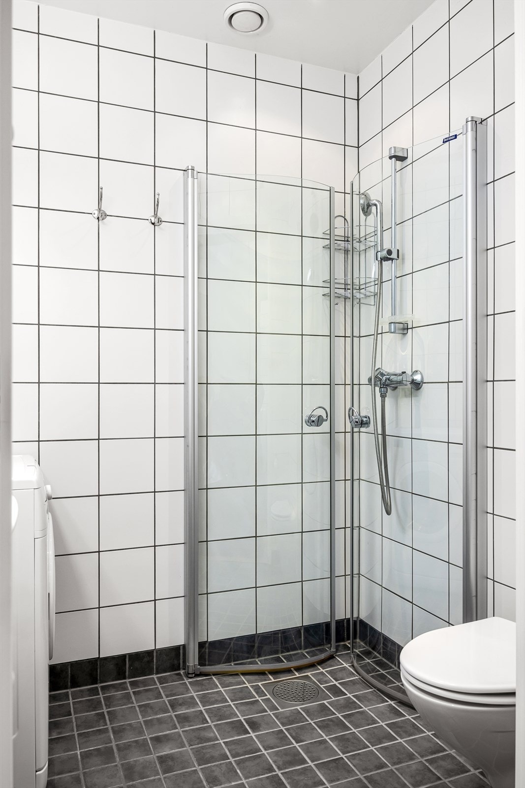 Badet består av servant, skap, speil og belysning. Videre er det dusjhjørne med vegg/dør i herdet glass og veggmontert toalett. Galleribilde