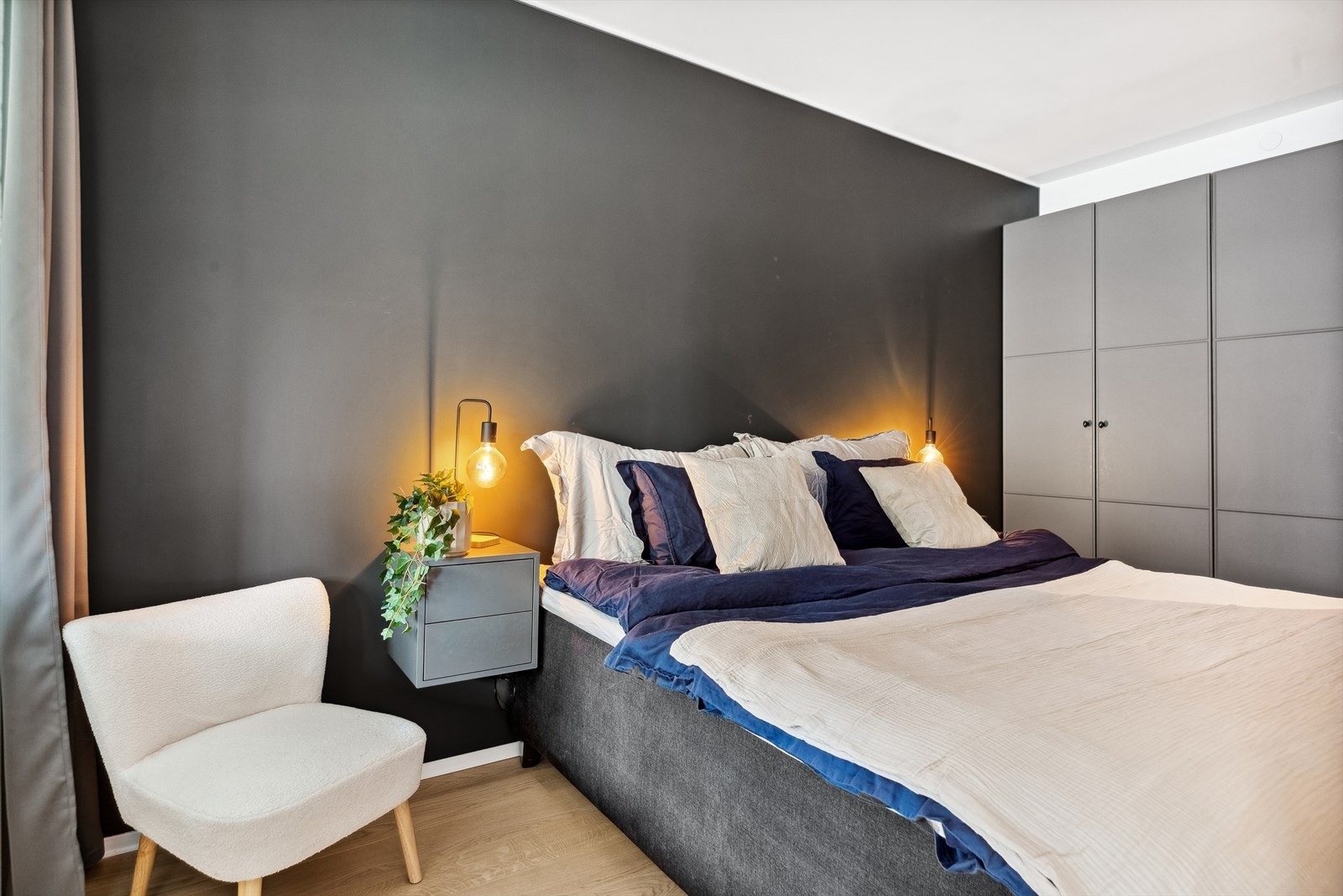 Soverommet har hvitmalte overflater, en koksgrå kontrastvegg og gyllen, enstavs parkett på gulvet. Galleribilde