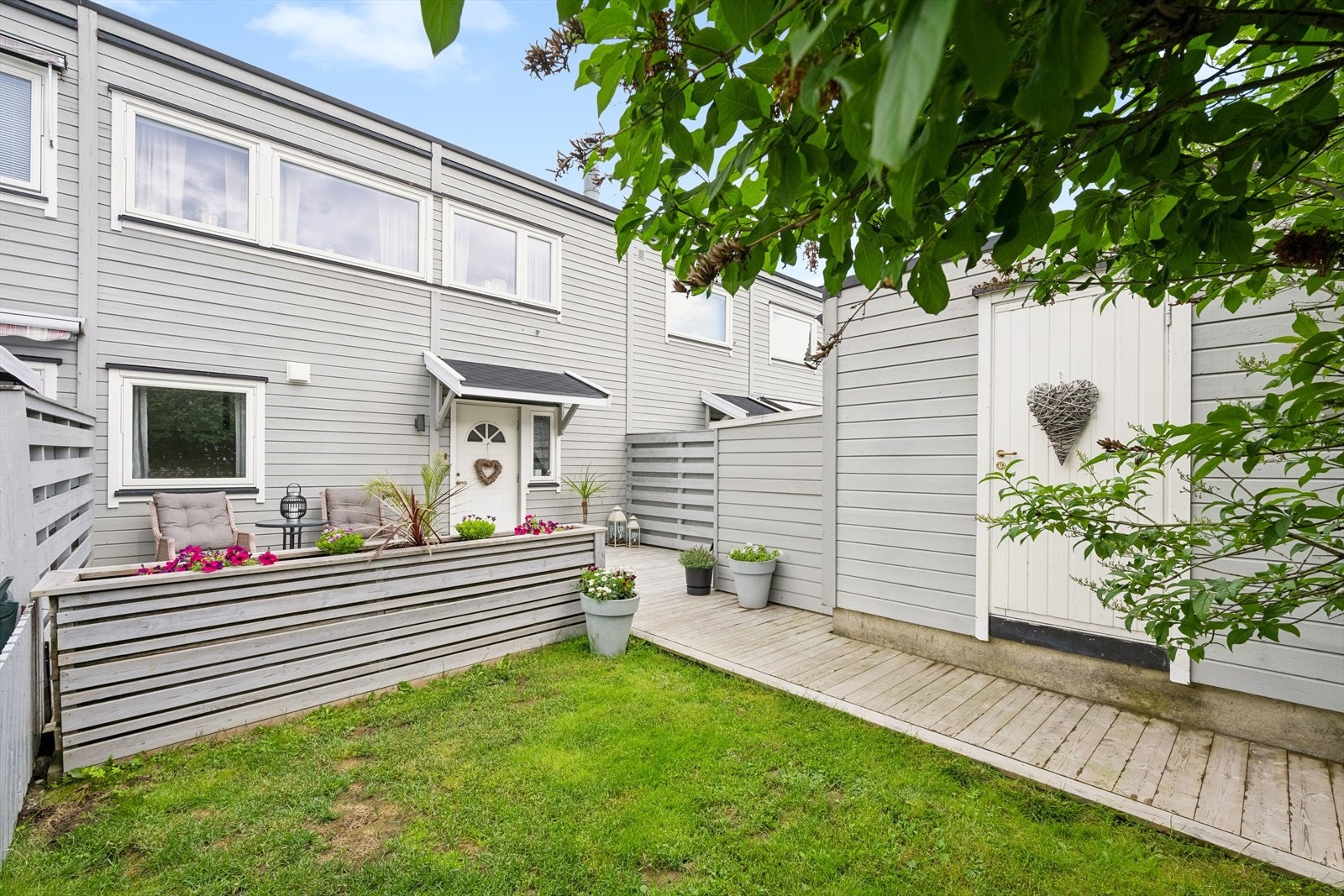 På forsiden av boligen er det en pent opparbeidet tomt med både noe gressplen, noe prydbusker som skjermer godt, og en flott platting som er skjermet med en fin plantekasse. Galleribilde