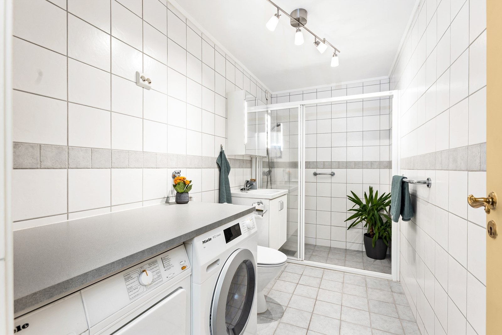 Flislagt bad med elektriske varmekabler i gulv. Servantinnredning med underskap, overskap med speil, gulvstående toalett og dusjhjørne med glassdører. Det er opplegg for og plass til vaskemaskin og tørketrommel, som medfølger handelen. Mekanisk avtrekk. Galleribilde