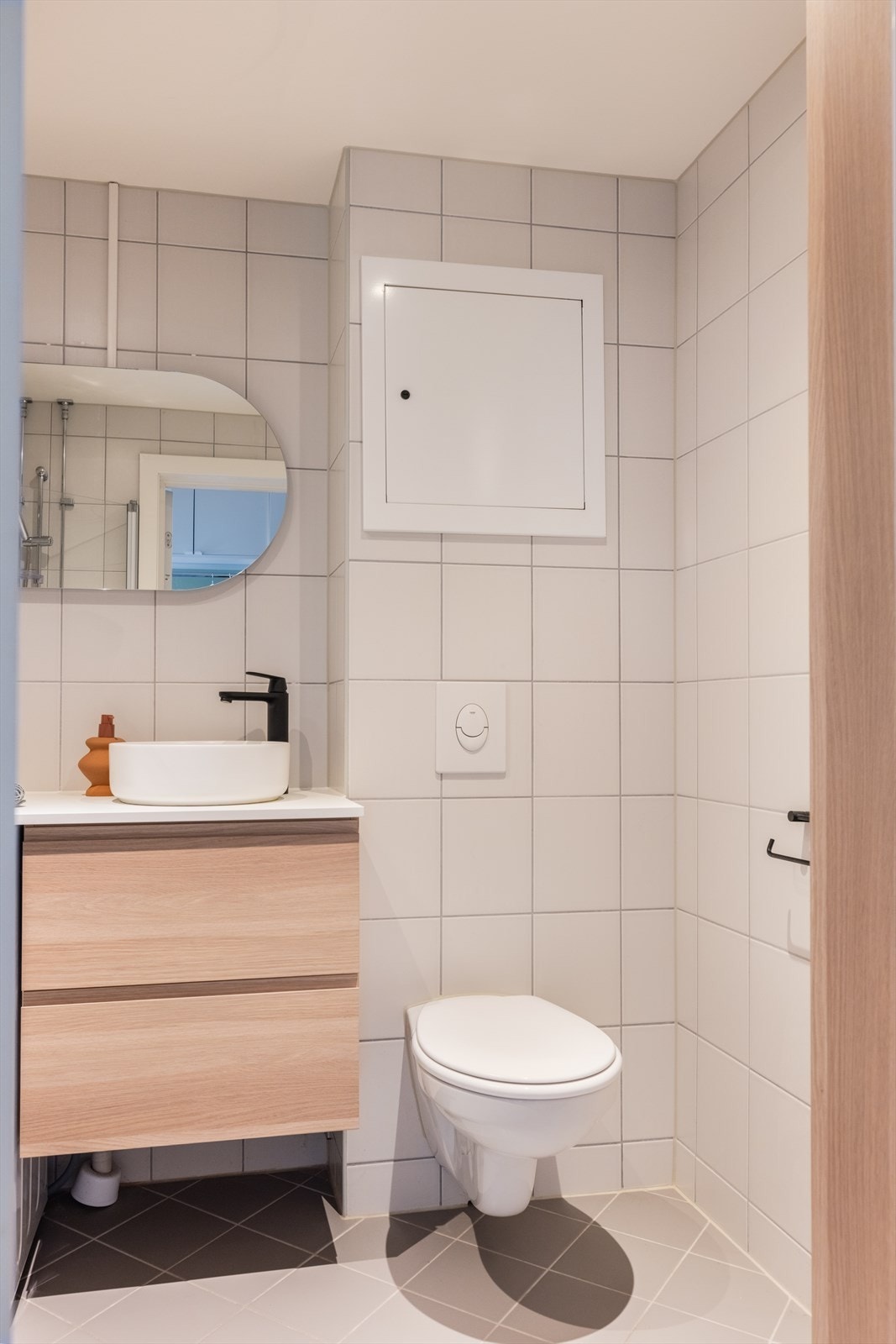 Badet inneholder høyskap og servantinnredning, laminert benkeplate, keramisk vask, ettgreps servantarmatur, speil med belysning og vegghengt toalett. Videre er det dusjhjørne med innfellbare dører Galleribilde