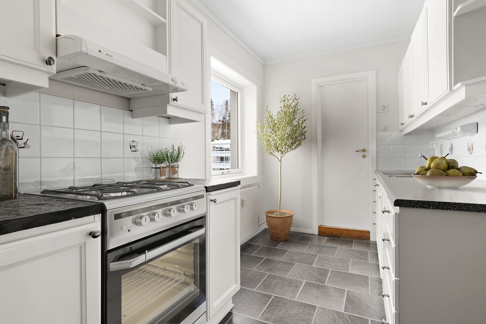 Keramiske benkeplater ved komfyr. Flislagt vegg mellom benkeskap og overskap. Innredning er beregnet for frittstående hvitevarer. Galleribilde