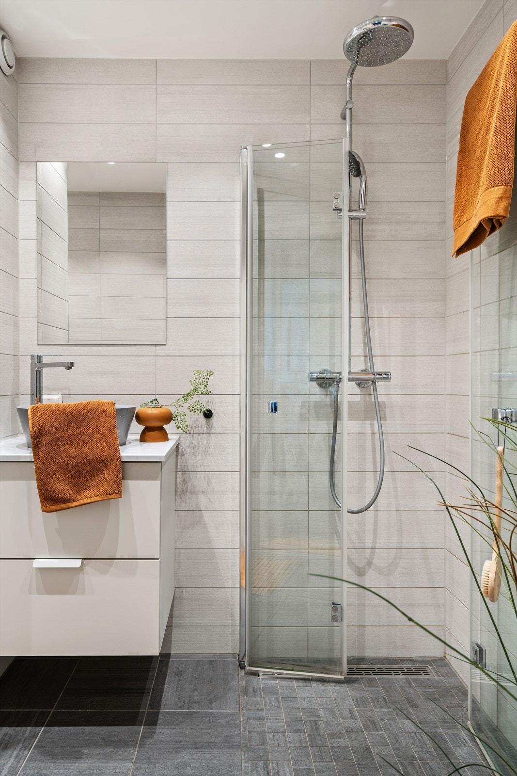 Innredning på badet består av veggmonterte dusjdører, bolleservant med underskap, speil og veggmontert wc. Galleribilde