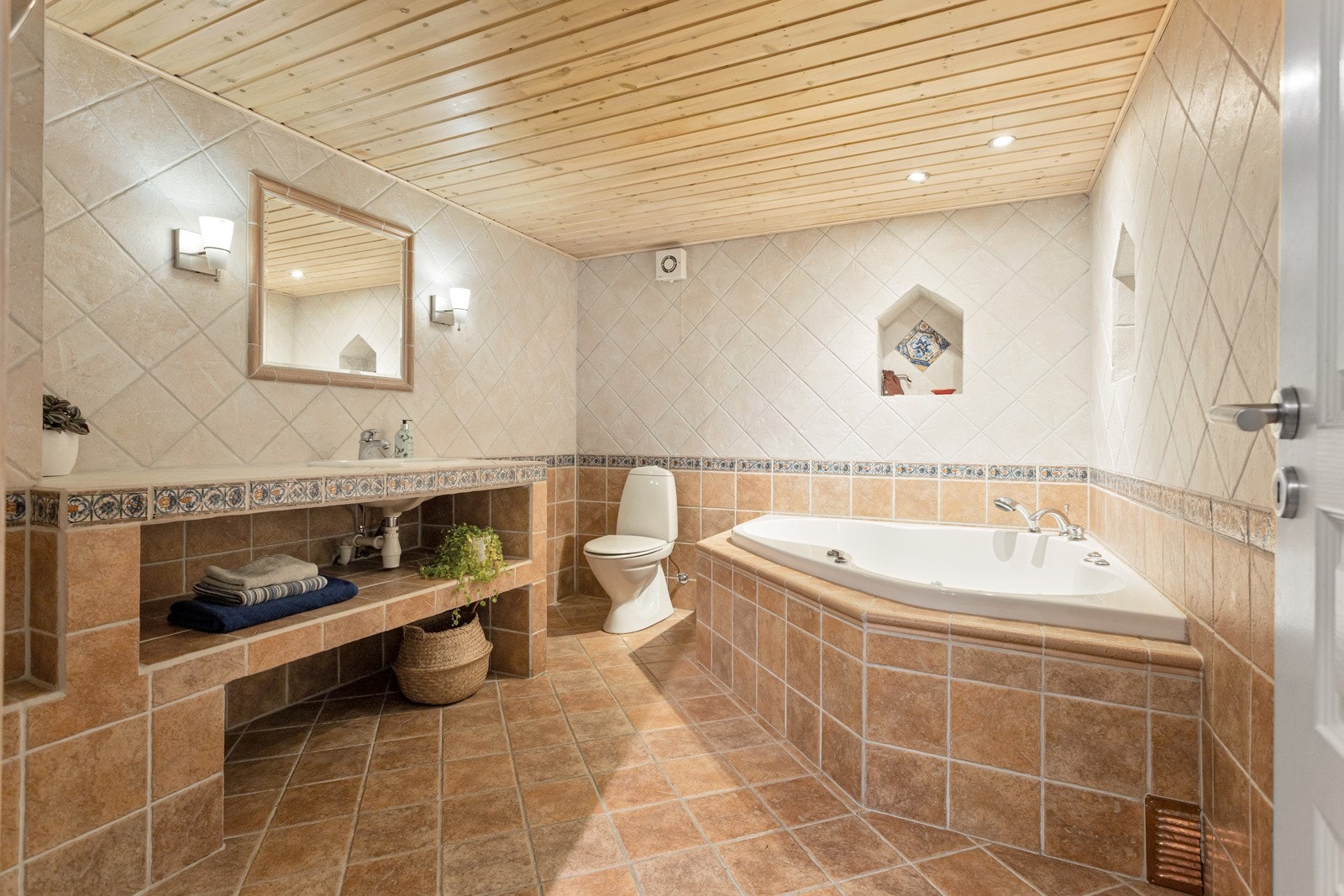 Badet innredet med flislagt benk med servant, innebygd badekar og toalett. Galleribilde