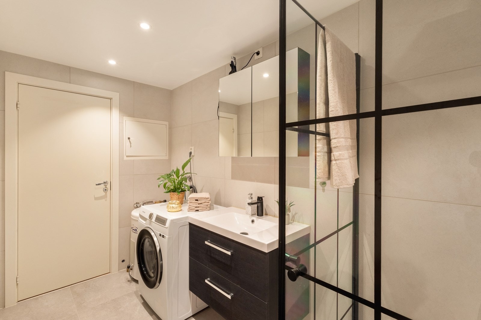 Badet er innredet med innfelbart dusjhjørne, dusjnisje, servant med underskuffer, speil med belysning, vegghengt toalett og opplegg for vaskemaskin Galleribilde