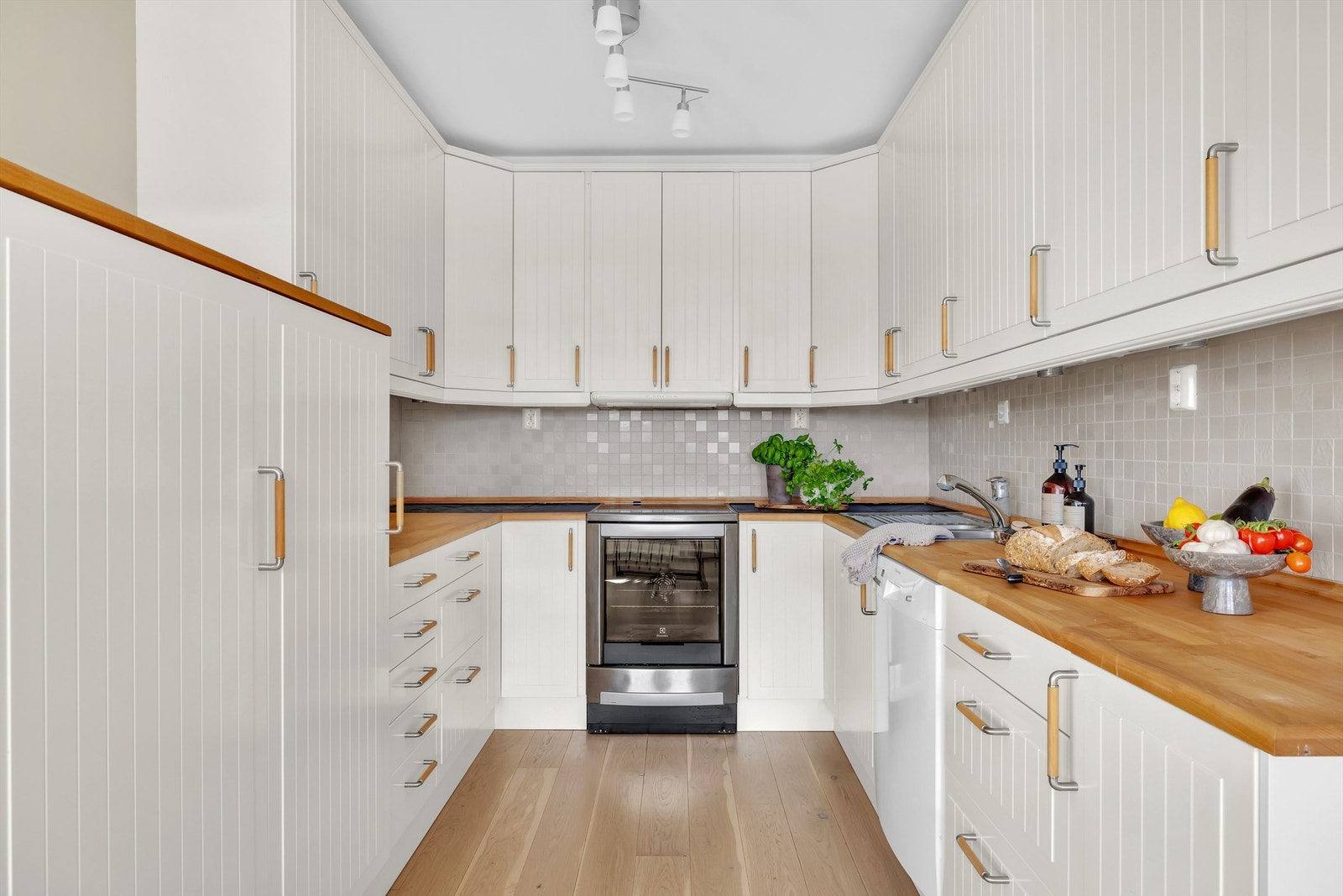 Kjøkkenet er lyst med profilerte fronter. Benkeplate av tre og fliser over kjøkkenbenk. Galleribilde