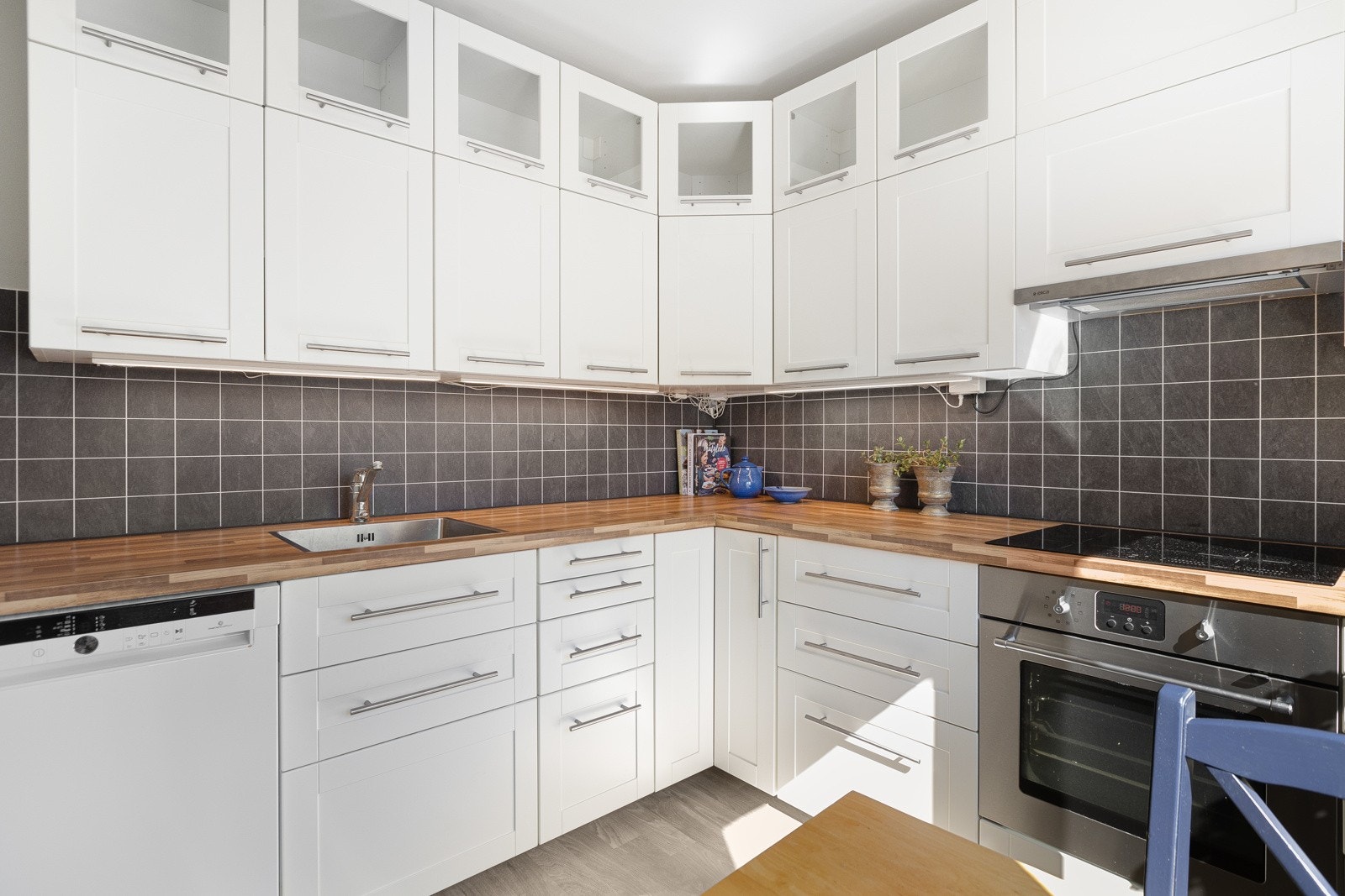 IKEA kjøkkenet fra 2013/14 har hvite, profilerte fronter på over- og underskap, hvor øvre rekke med overskap har dører i glass, og laminert benkeplate. Galleribilde