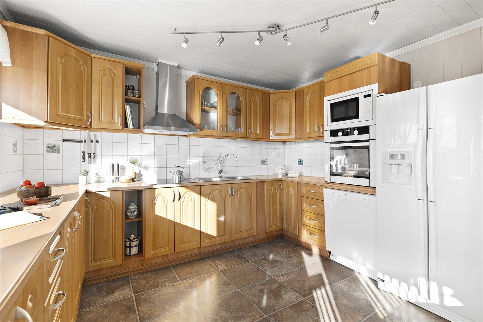 Klassisk kjøkken fra 2006. Innredningen består av profilerte fronter, laminat benkeplate med nedfelt kum i rustfritt stål, belysning under overskap og fliser på vegg over benkeskap Galleribilde