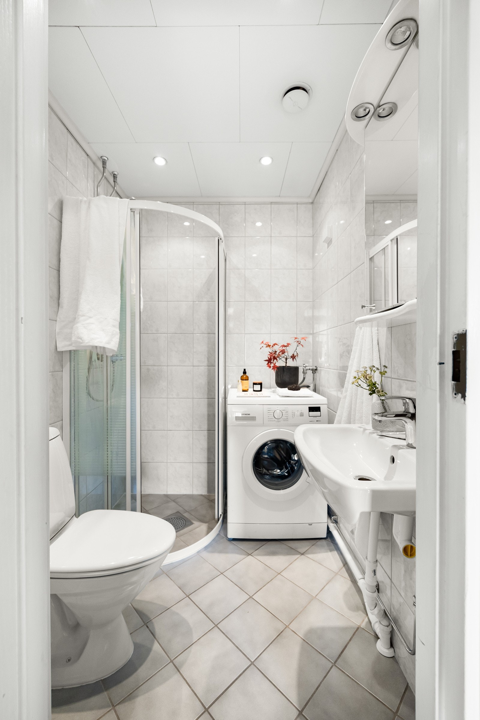 Flislagt baderom med dusjnisje, gulvstående toalett, servant og opplegg for vaskemaskin. Galleribilde