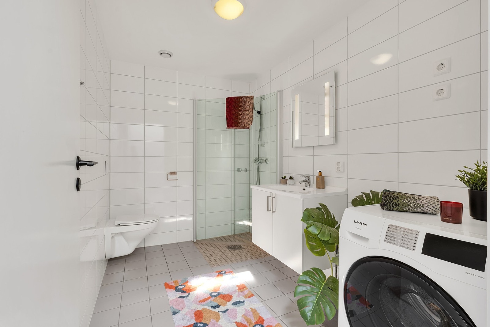 Badet har flislagte flater og varmekabler i gulv. Dusjhjørne, vegghengt WC og opplegg for vaskemaskin. Galleribilde