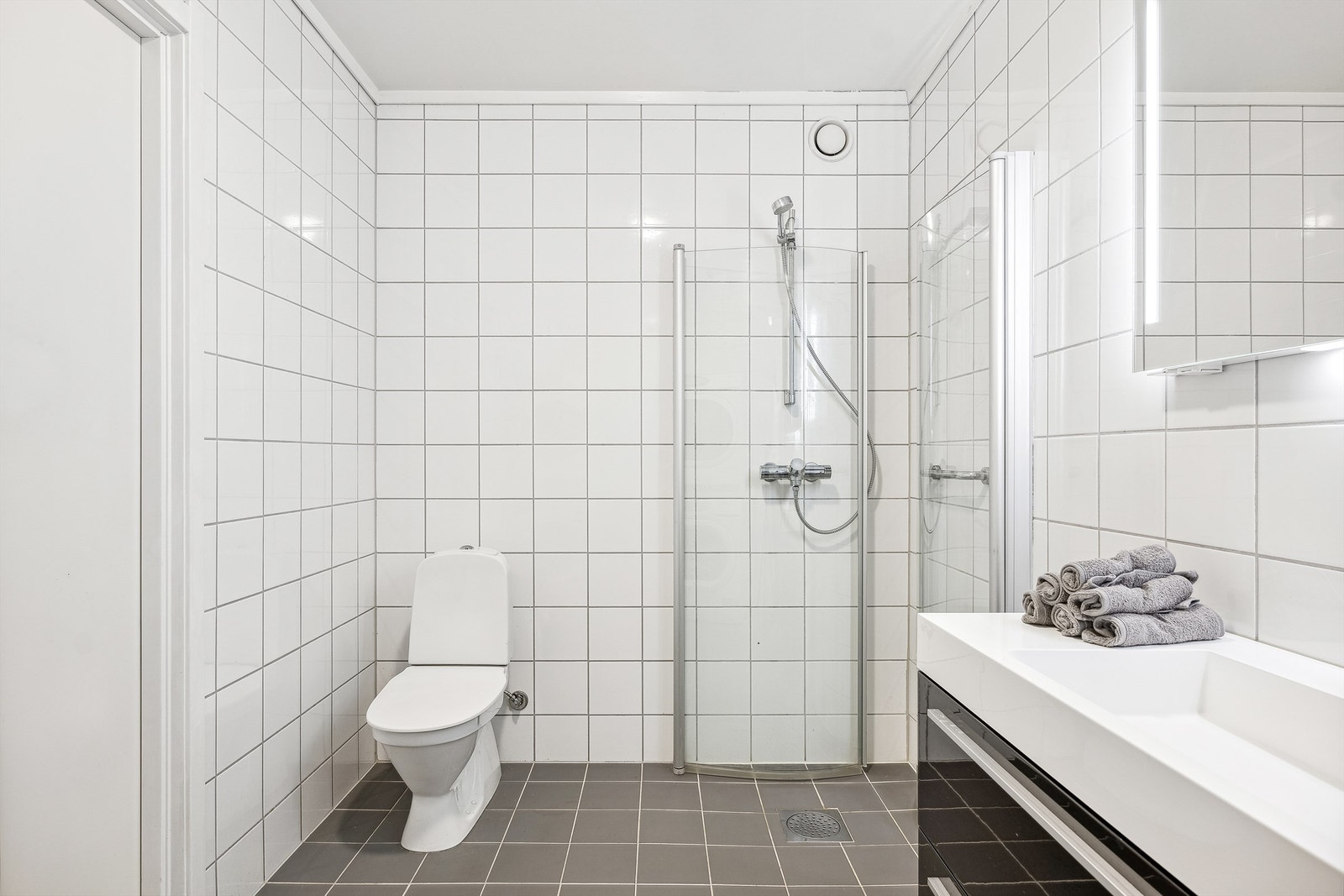 Badet har dusj montert på vegg med praktiske innfellbare dusjvegger Galleribilde