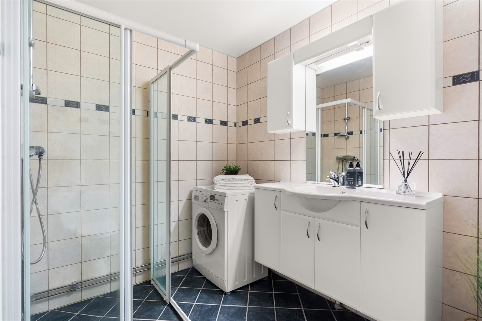 Badet har lyse veggfliser, mørke gulvfliser og gulvvarme. Vaskemaskin medfølger. Galleribilde