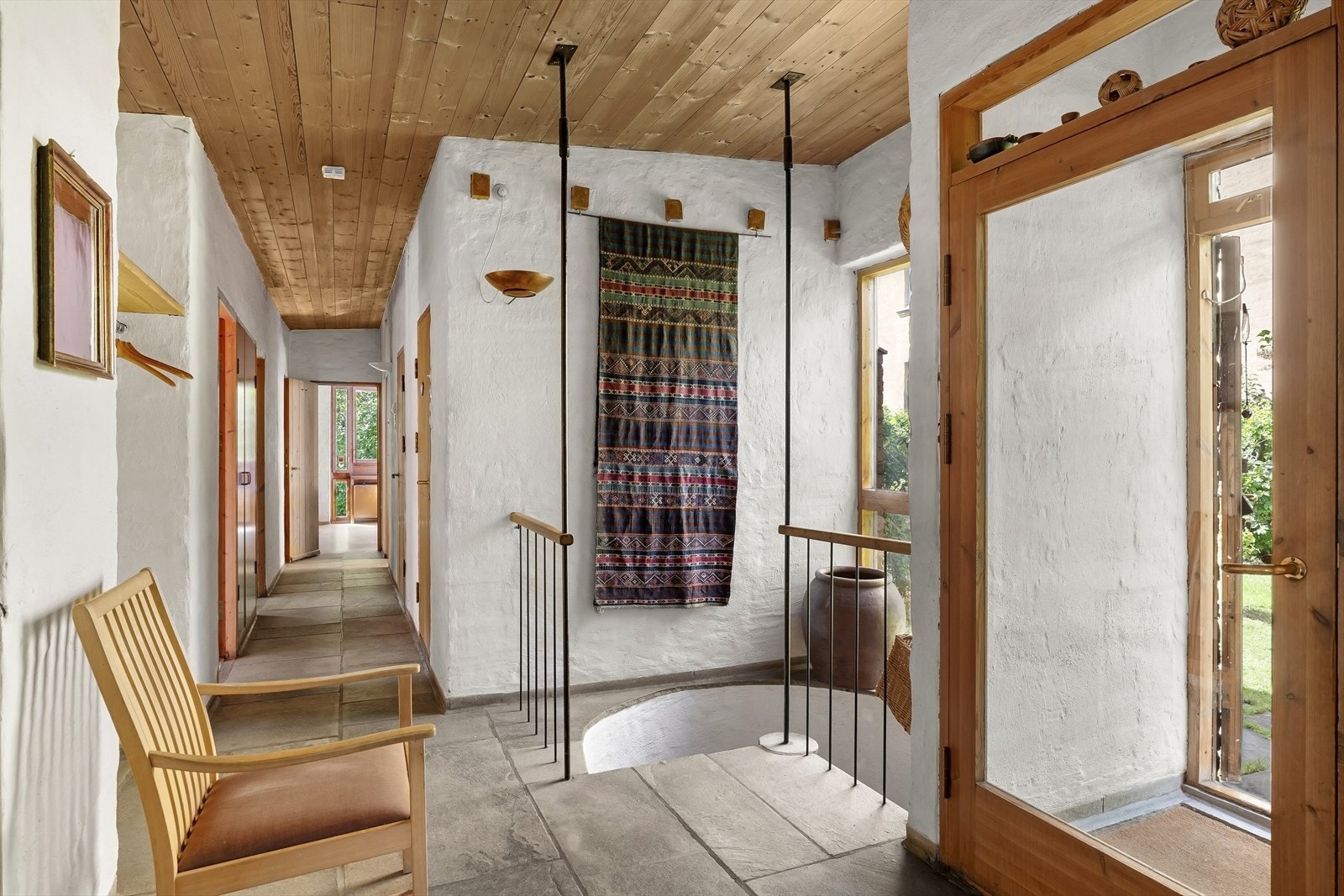 Hallen sett mot soveromsfløyen. Egen nisje for å henge fra seg yttertøy til venstre i bildet. Støpt vindeltrapp med skifer i trinn. Galleribilde